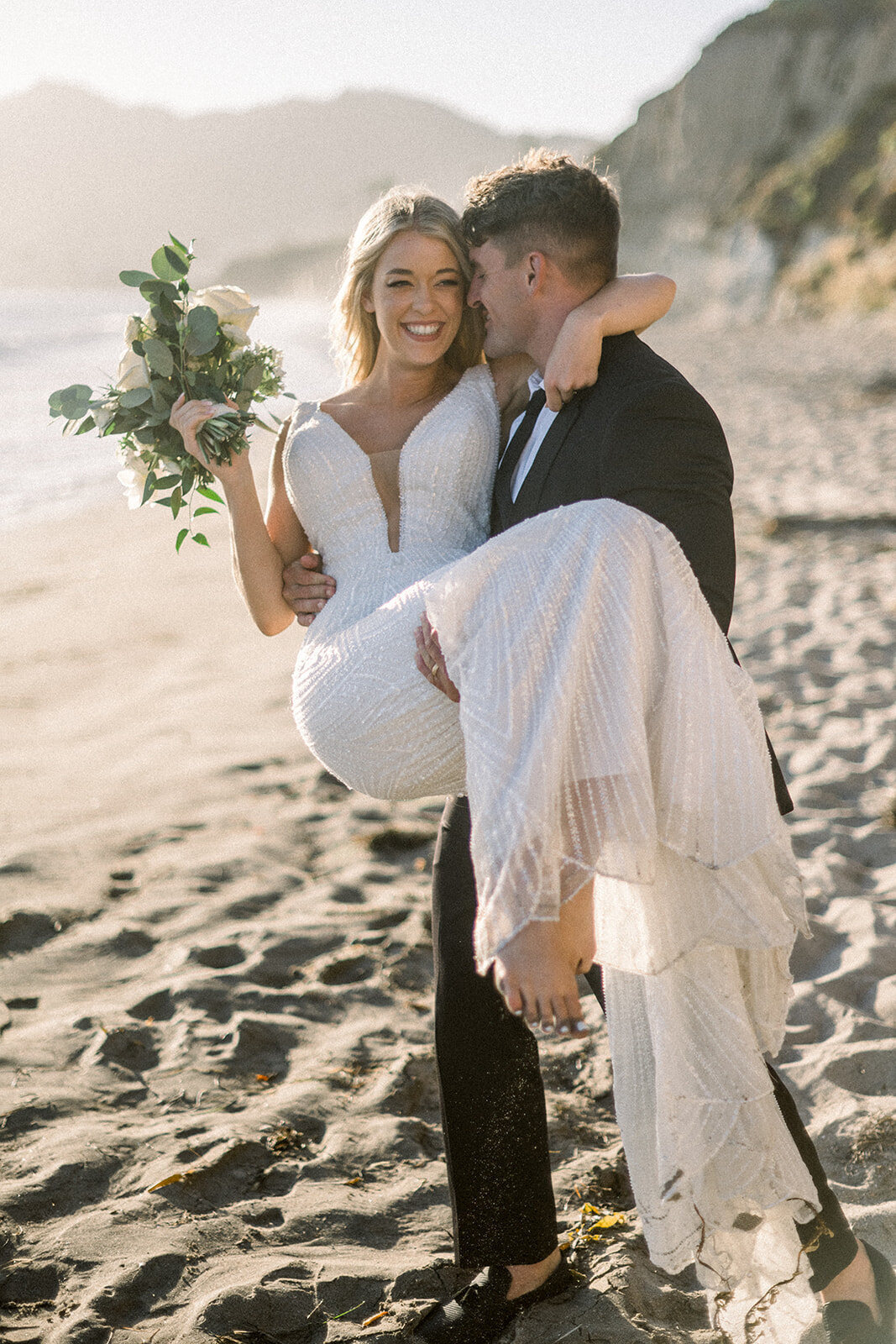 Groom carrying bride on the beach at Dolphin Bay Resort wedding in Pismo Beach, CA