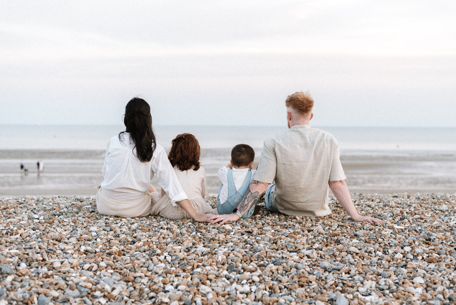 Mum and dad with their two children sitting and looking at the sea during family photoshoot in Billingshurst