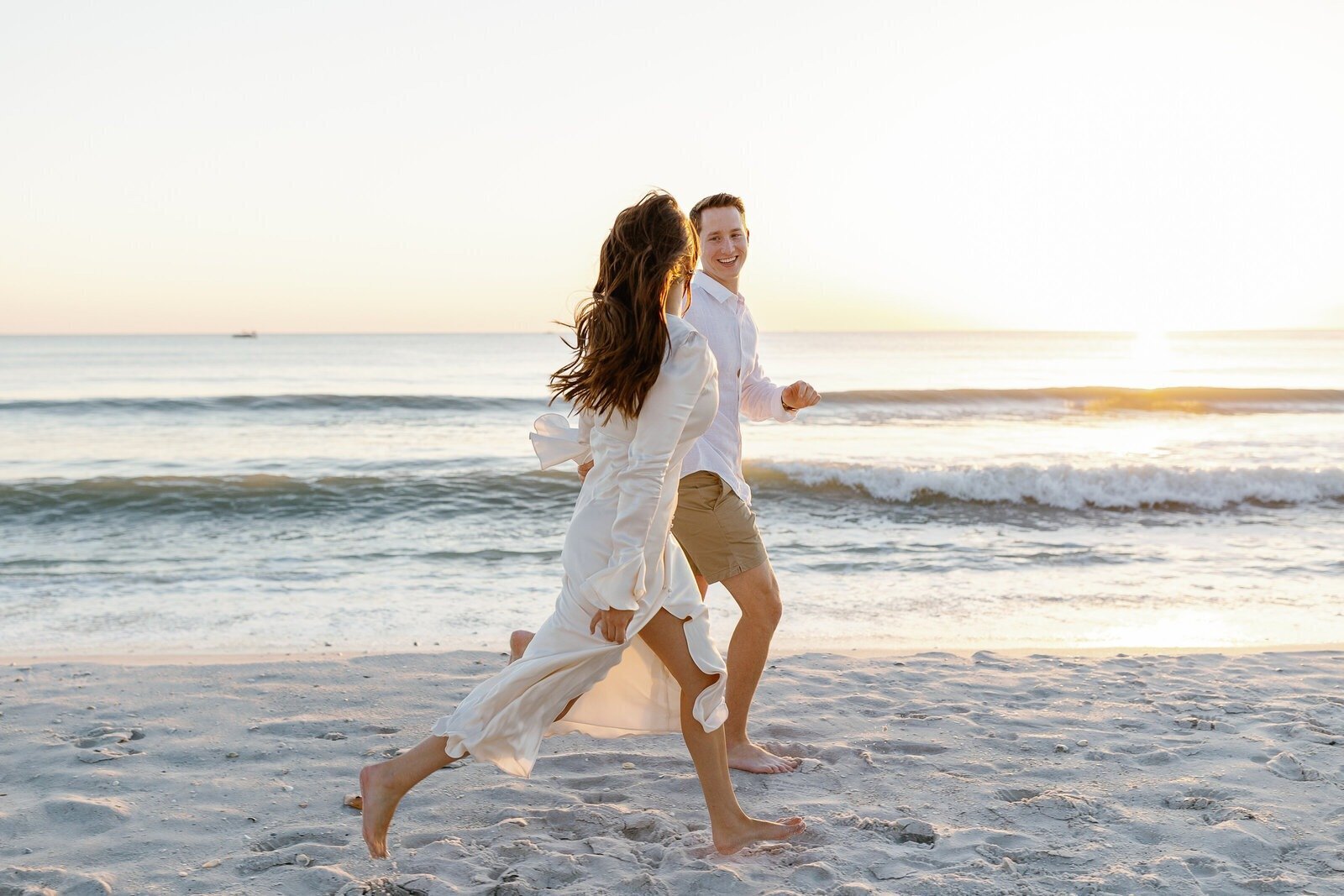 couple running across beach for their engagement photo session in Naples, Florida