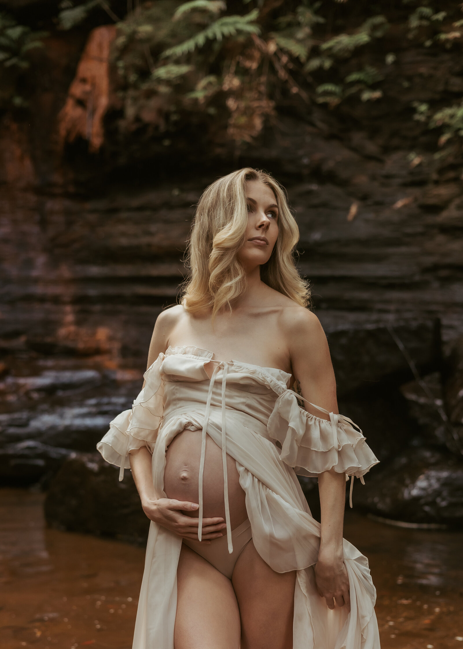 An outdoor maternity photoshoot at a gorgeous waterfall for this beautiful pregnant woman who is wearing a silk dress that shows off her growing baby bump.