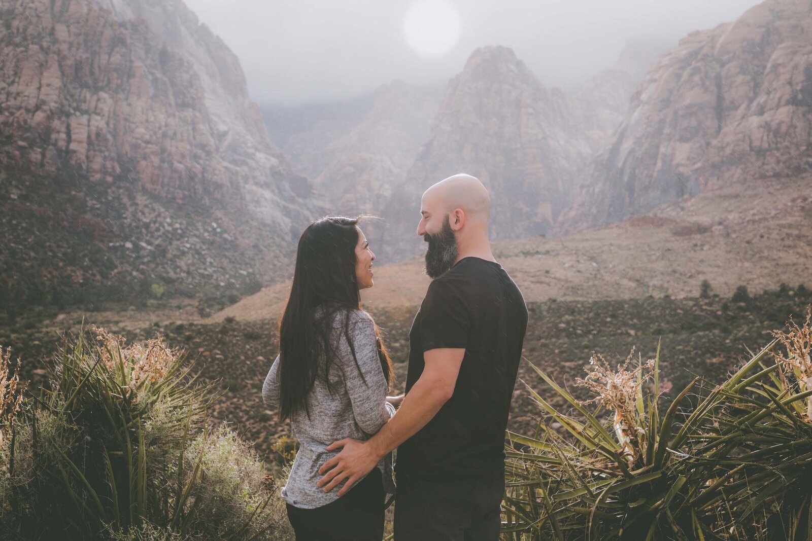 Couple looks at each other and smile among desert and mountain views.