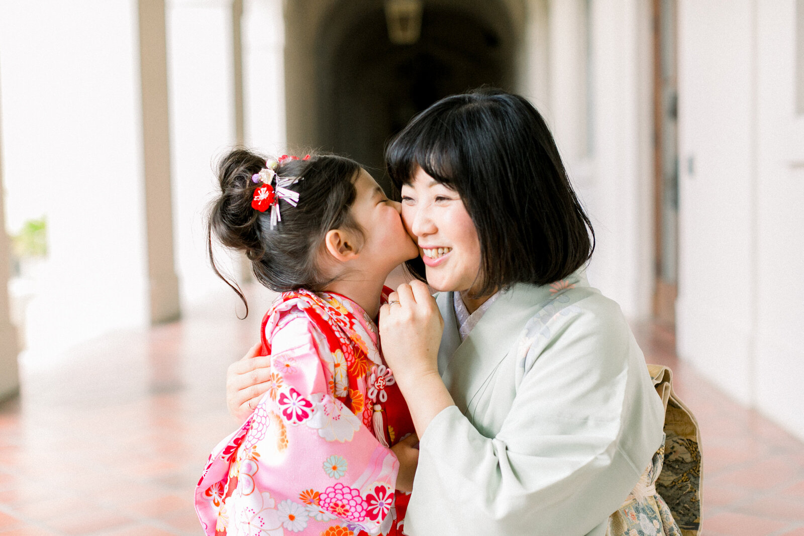Mother and daughter in kimono sharing a joyful kiss during Shichi-Go-San celebration in Pasadena | 七五三 母娘着物 ピンクとグリーン 親子のハグ＆キス パサデナ