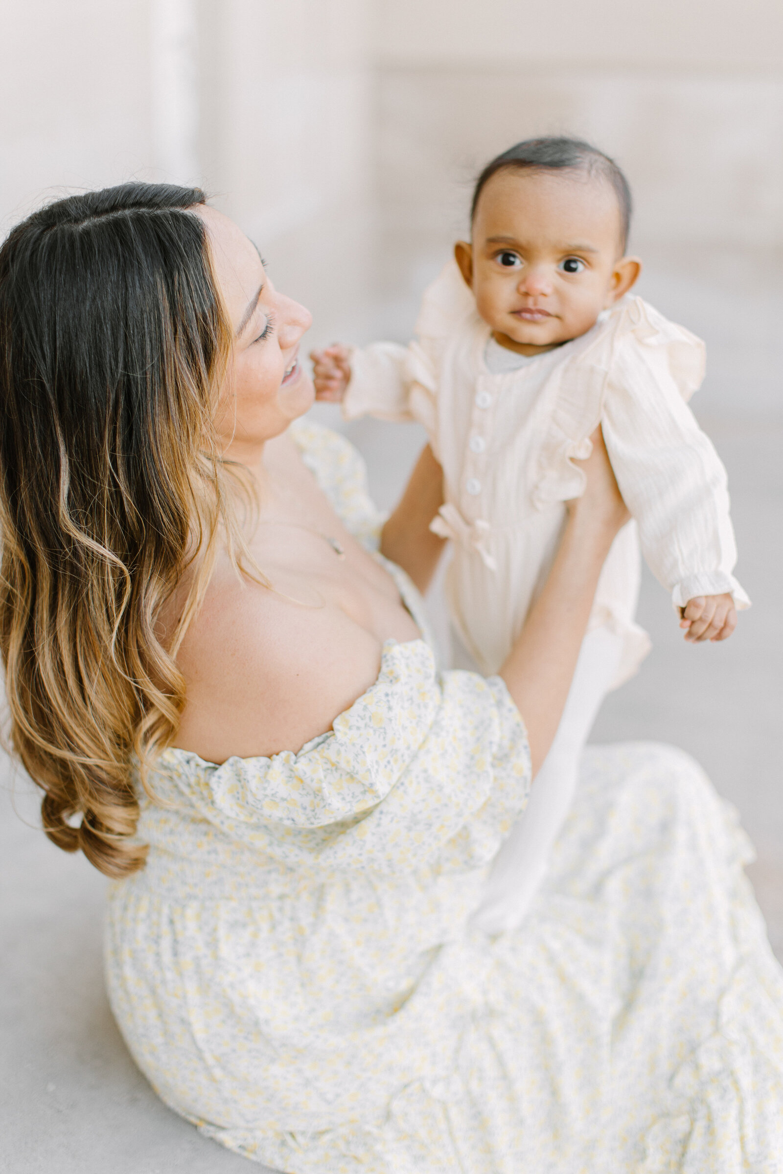 A young mother wearing an off the shoulder dress and holding her baby girl up during photo session with Boston newborn photographer Corinne Isabelle