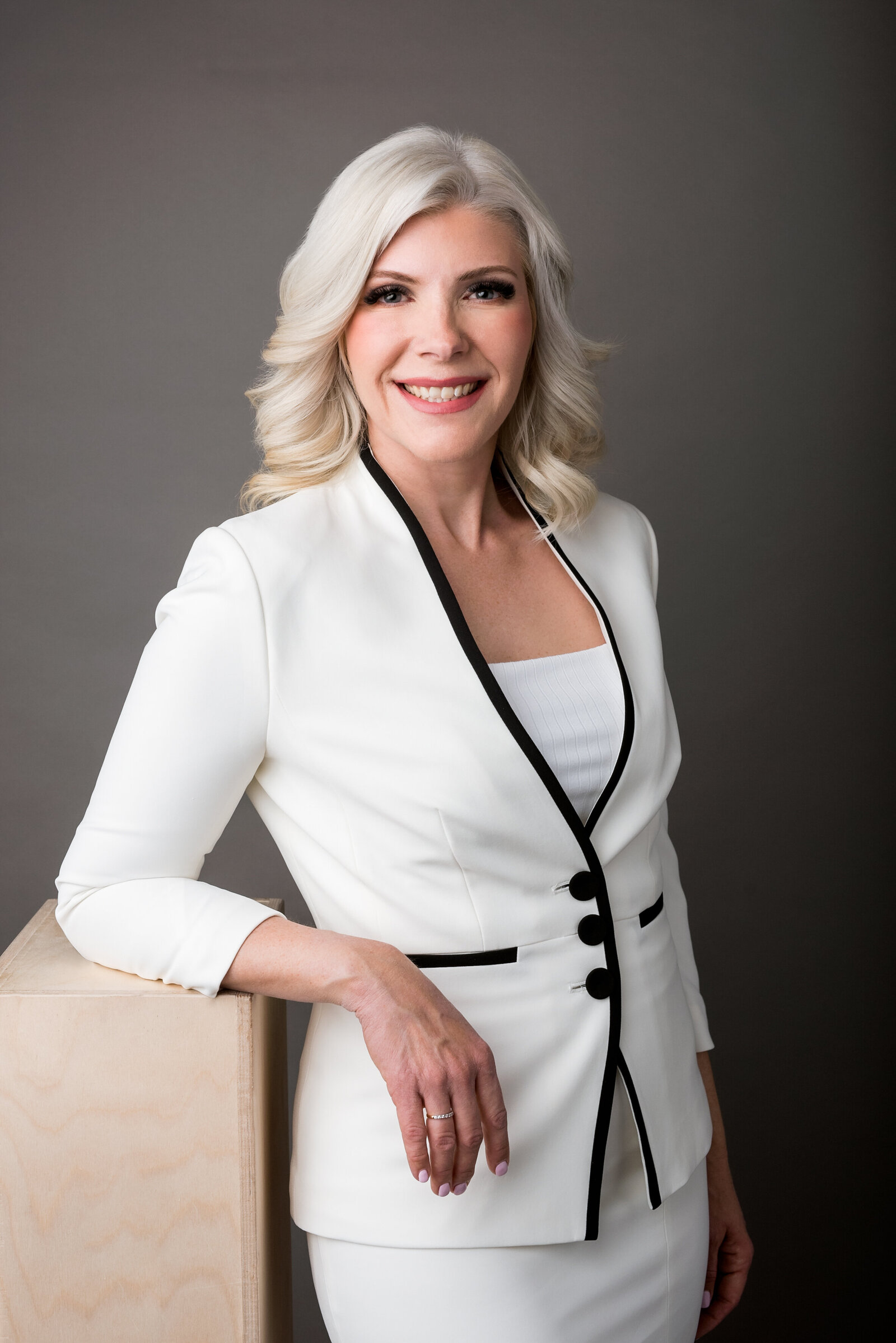 Headshot of an executive woman wearing designer white suit jacket with black piping and buttons