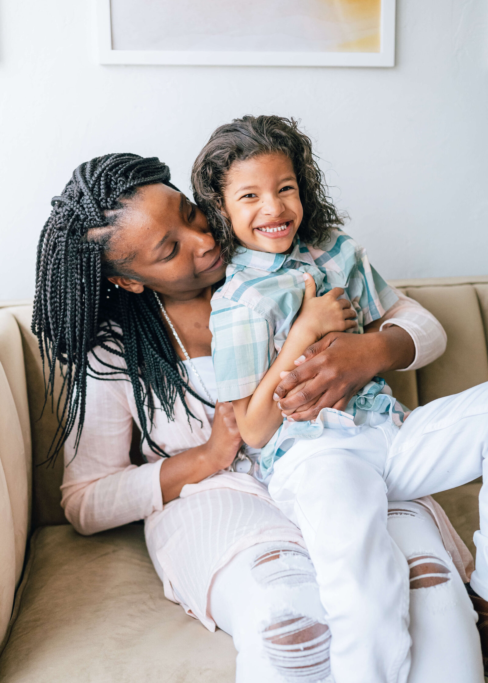 A mom dressed in pastels hugs and tickles her toddler son who is flashing the camera a bright, big smile