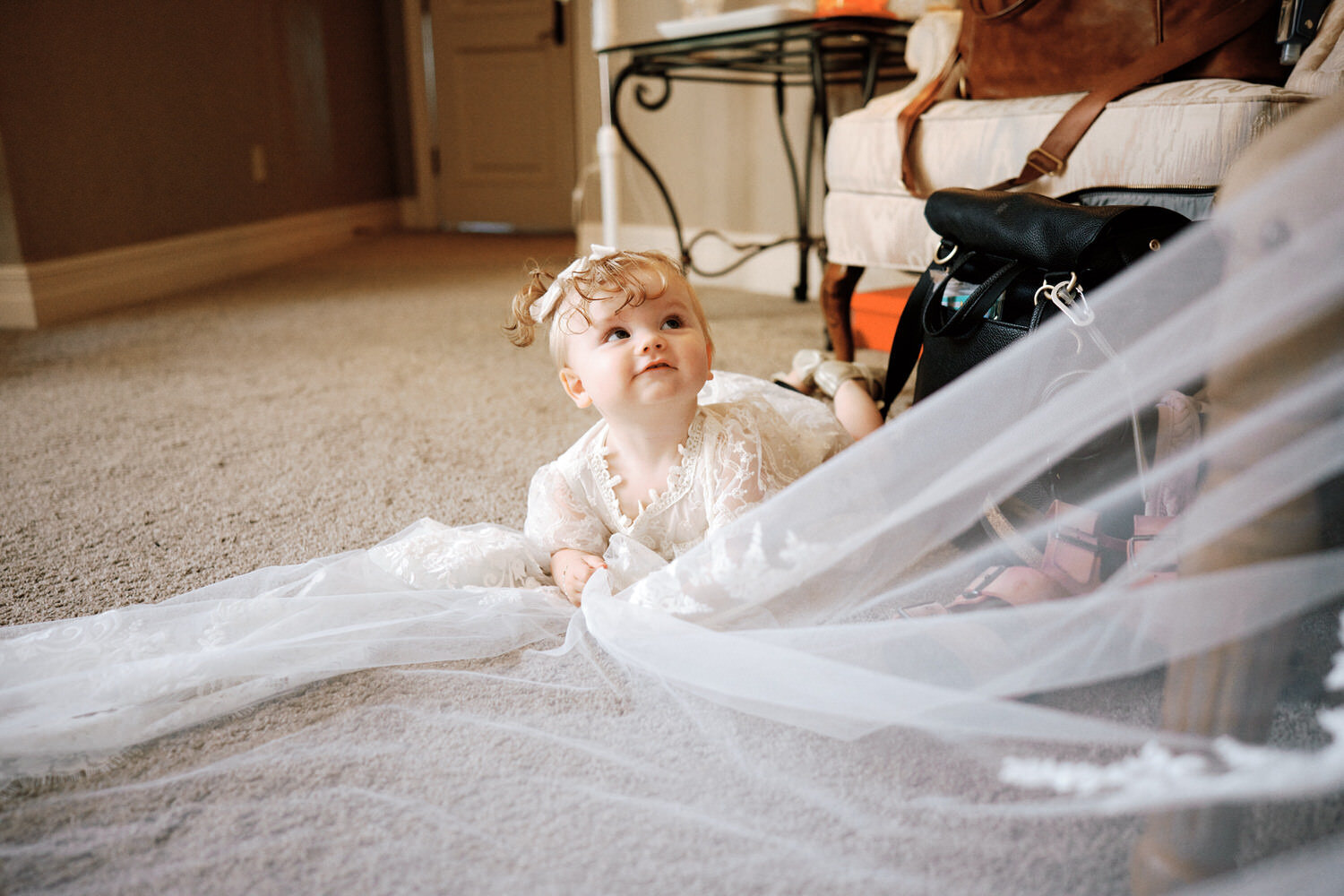 Baby grabs onto the bridal veil and looks up at the bride