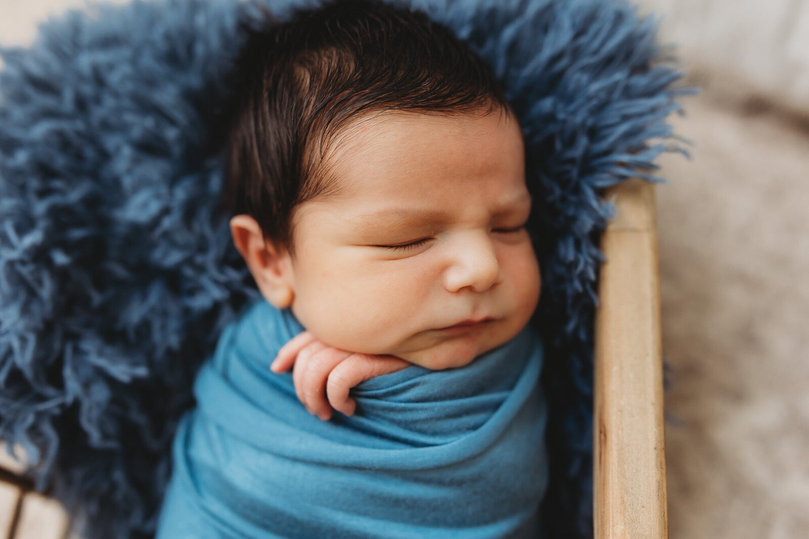 Baby boy with a full head of hair swaddled in blue sleeping during his newborn session