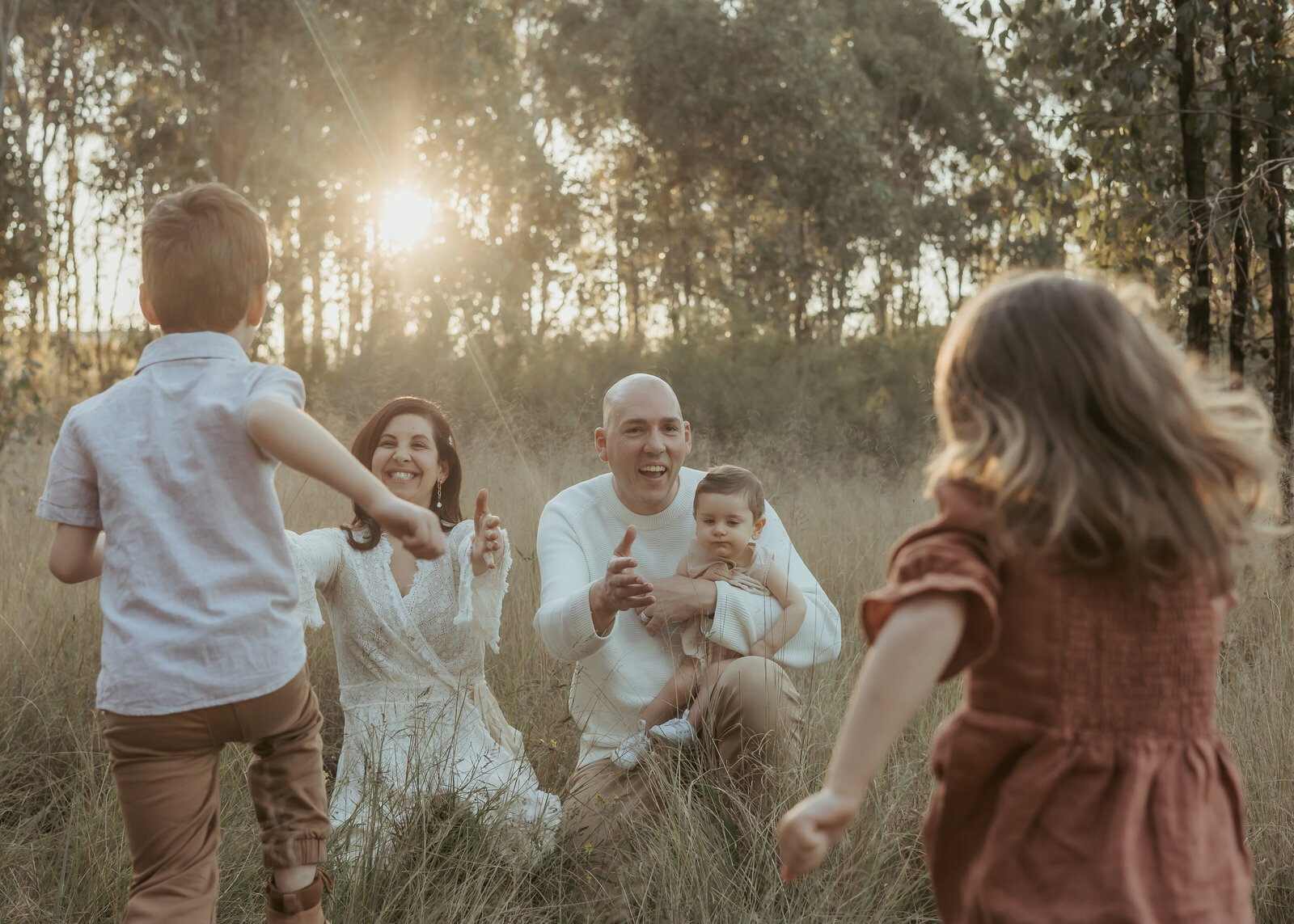 A family photoshoot in a beautiful Sydney grassy field at sunset where the kids are running to their parents for a cuddle.