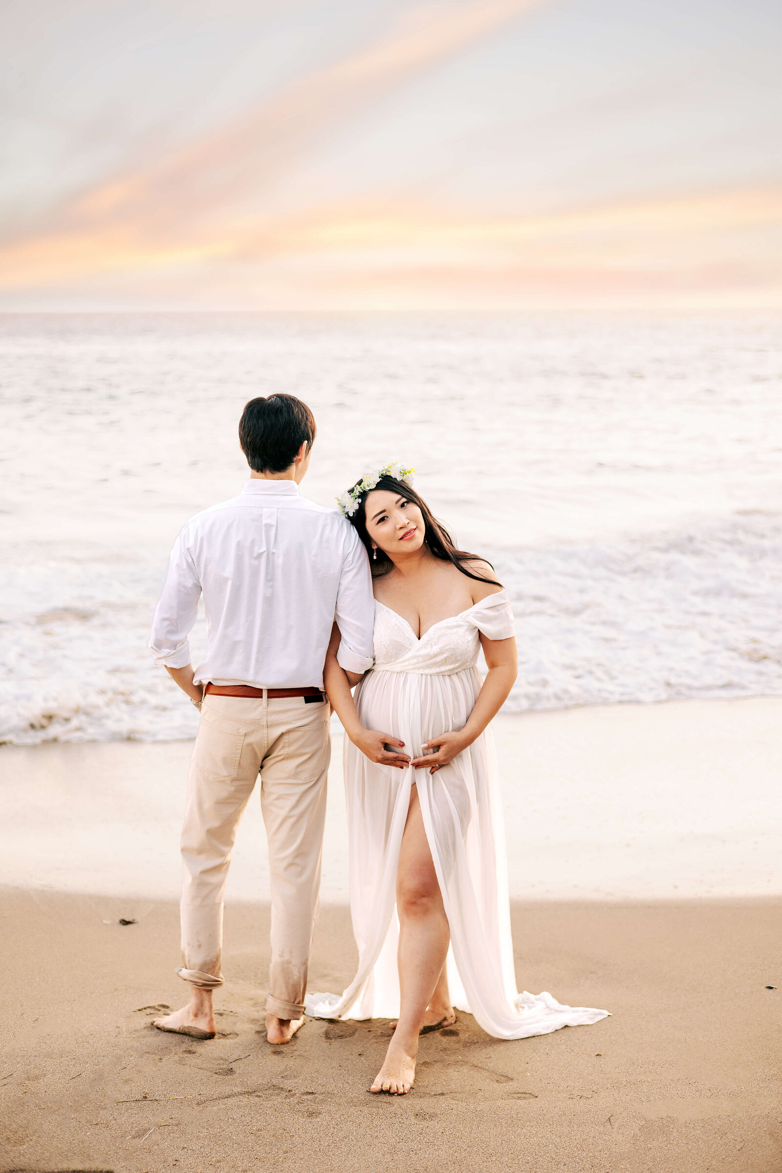 Expectant Mom resting head on her husbands shoulder while holoding her baby bump at Laguna Beach, CA maternity session.