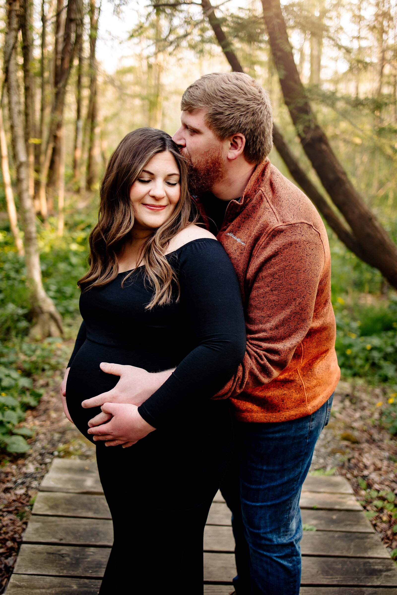 Husband cradles his wife's pregnant belly and kisses her forehead