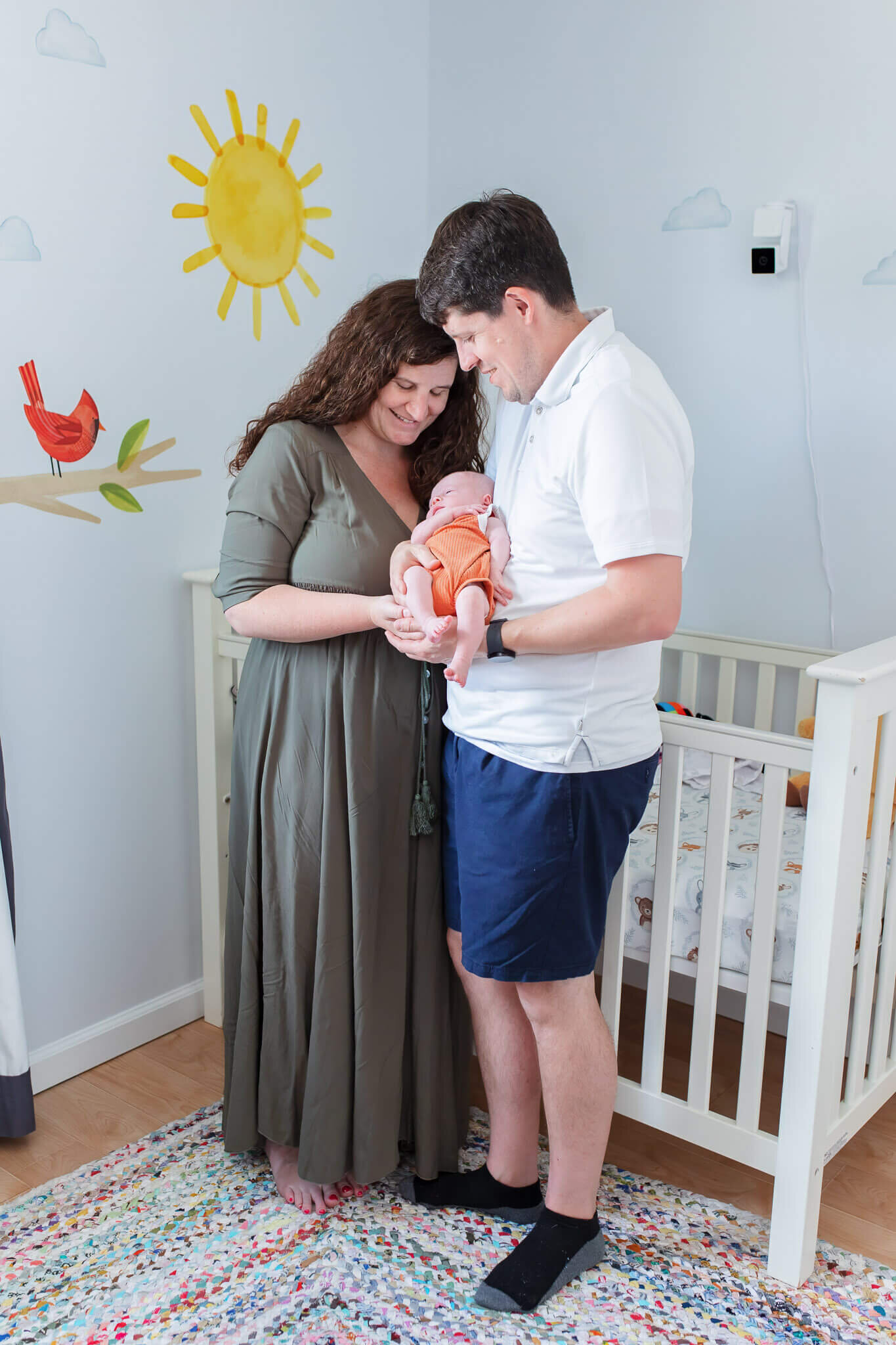 A mom and dad holding their newborn son standing in front of the crib.