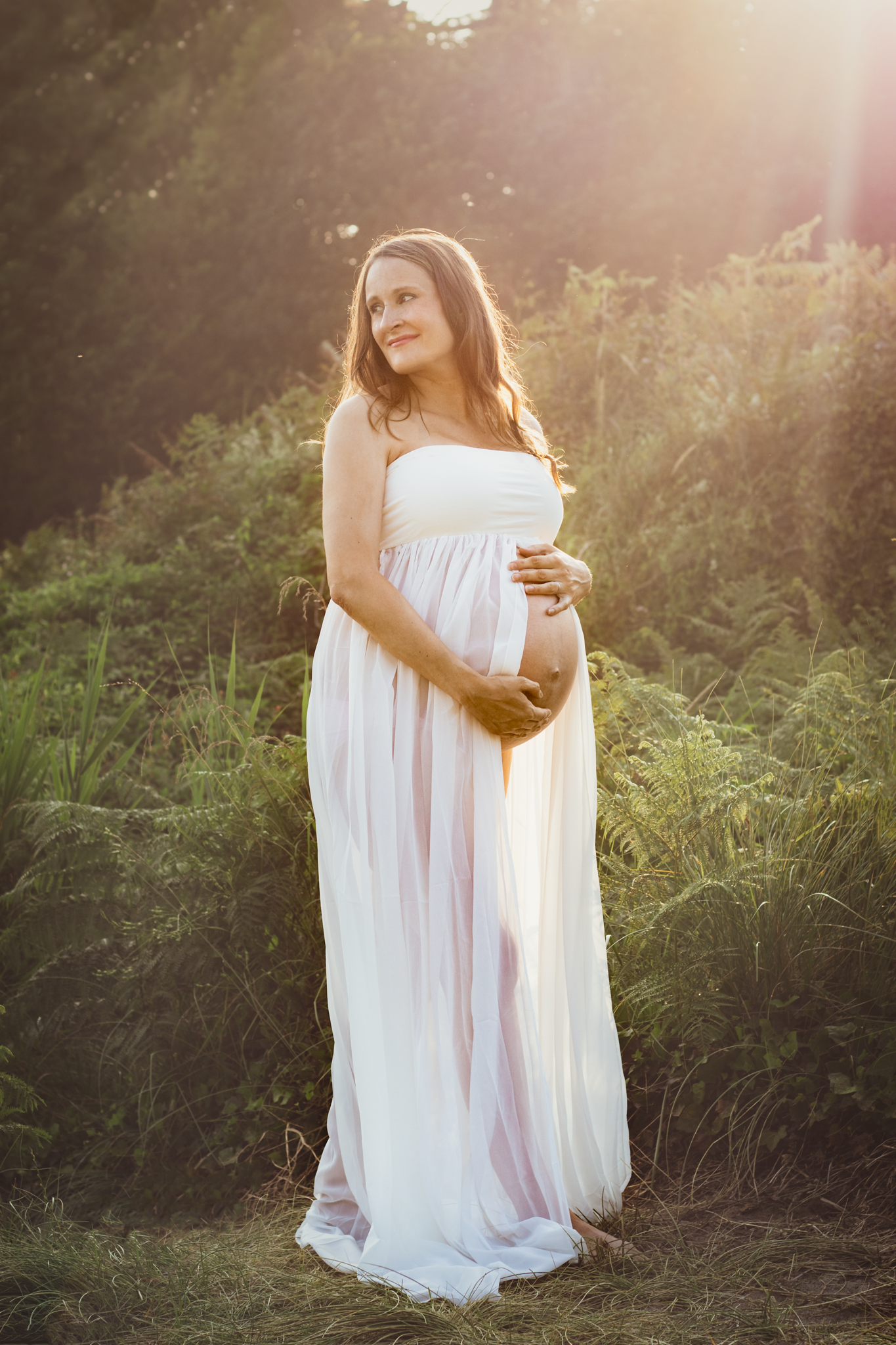 Woman wear white dress poses for Maternity Photoshoot on the beach in Devon
