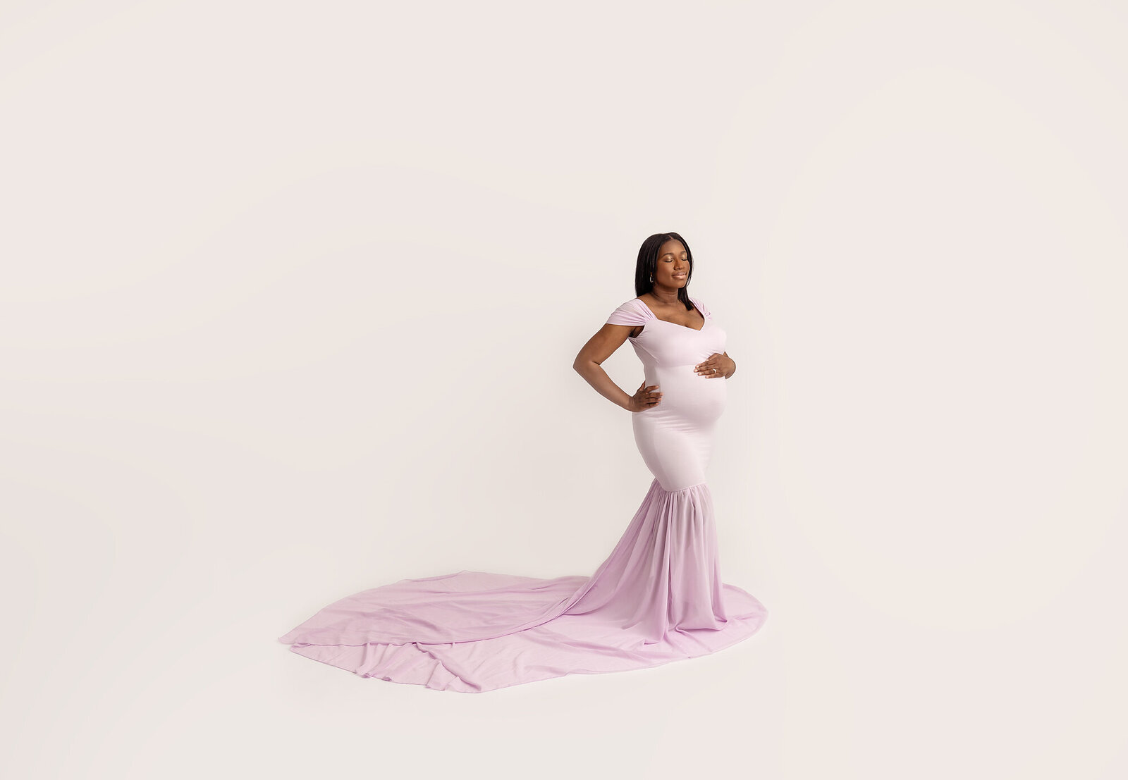 black woman in pink dress posing with hand on pregnant belly