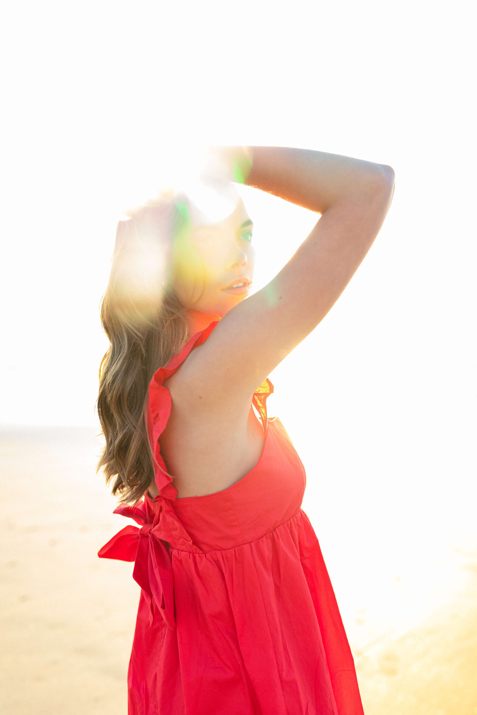 brunette high school girl posing in a red dress in front of the sun
