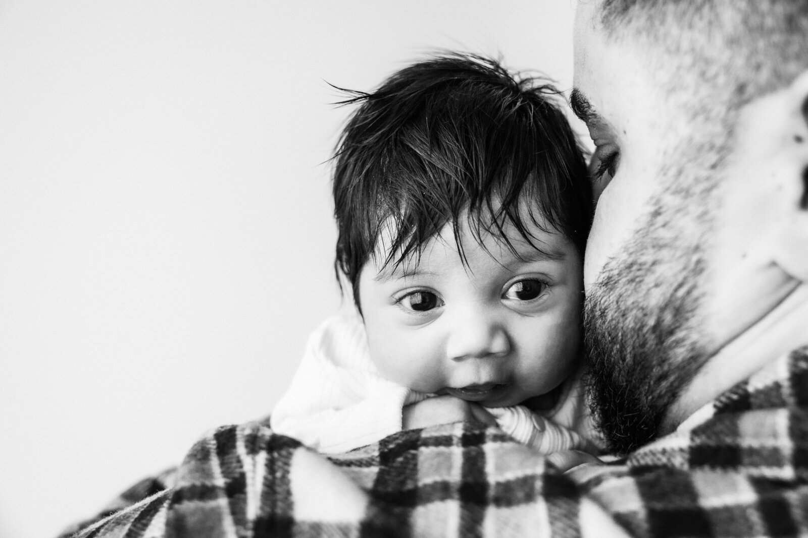 Black and white photo of newborn baby looking over dads shoulder