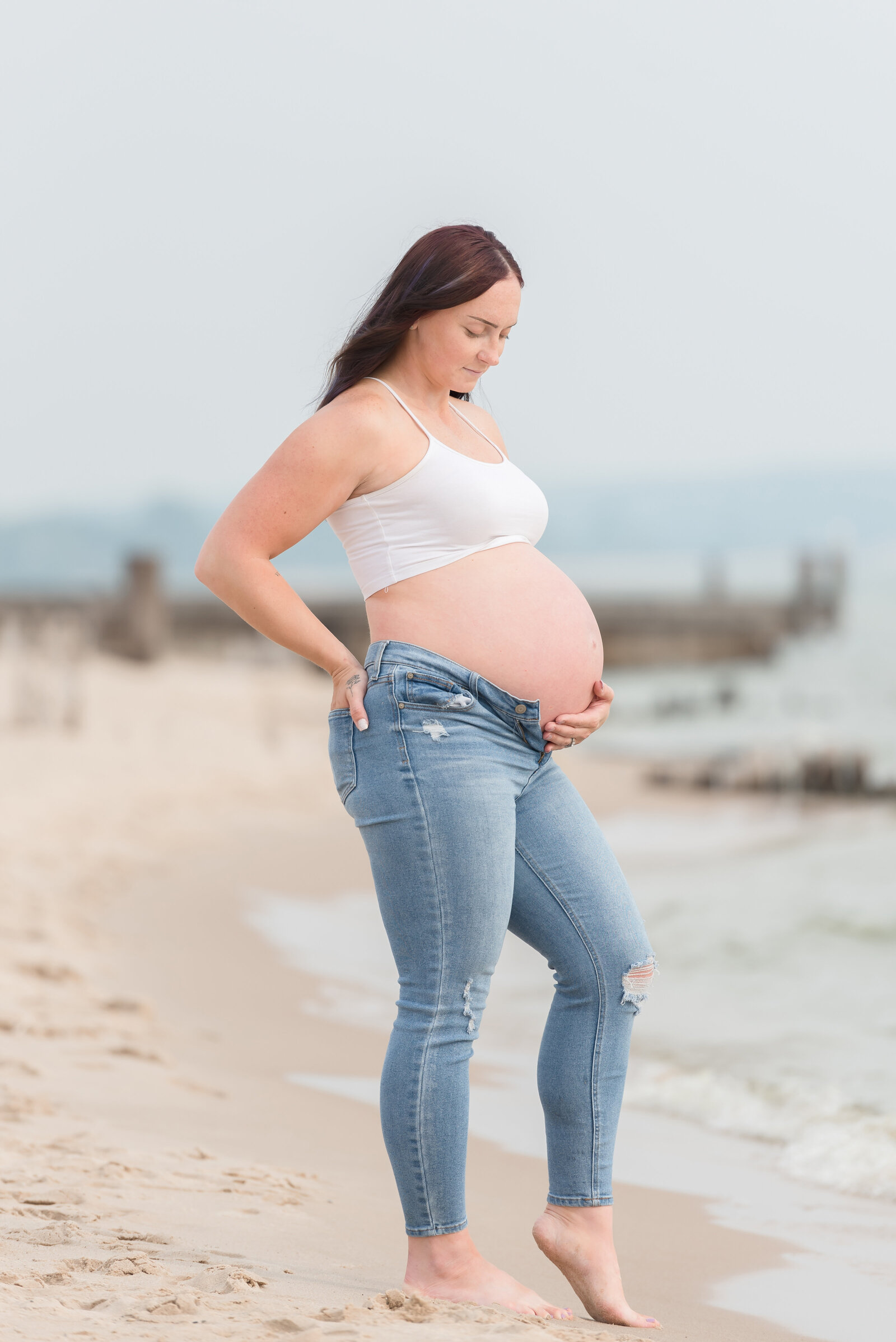 mother standing on beach in Ludington with her hand on her bump