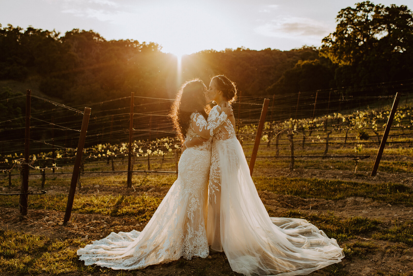Golden Hour LGBTQ brides kissing in matching dresses.