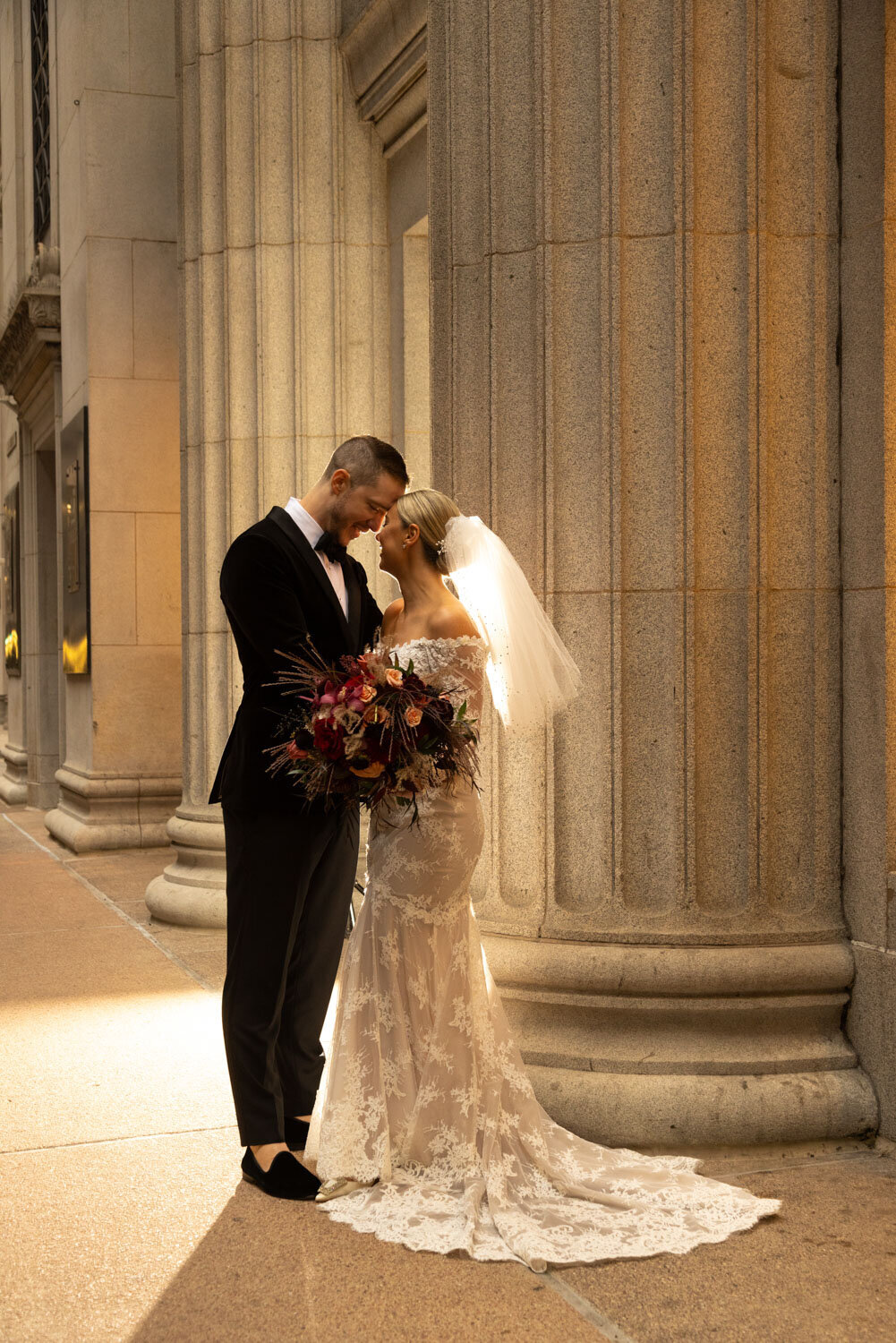 A bride and groom standing next to each other in front of columns