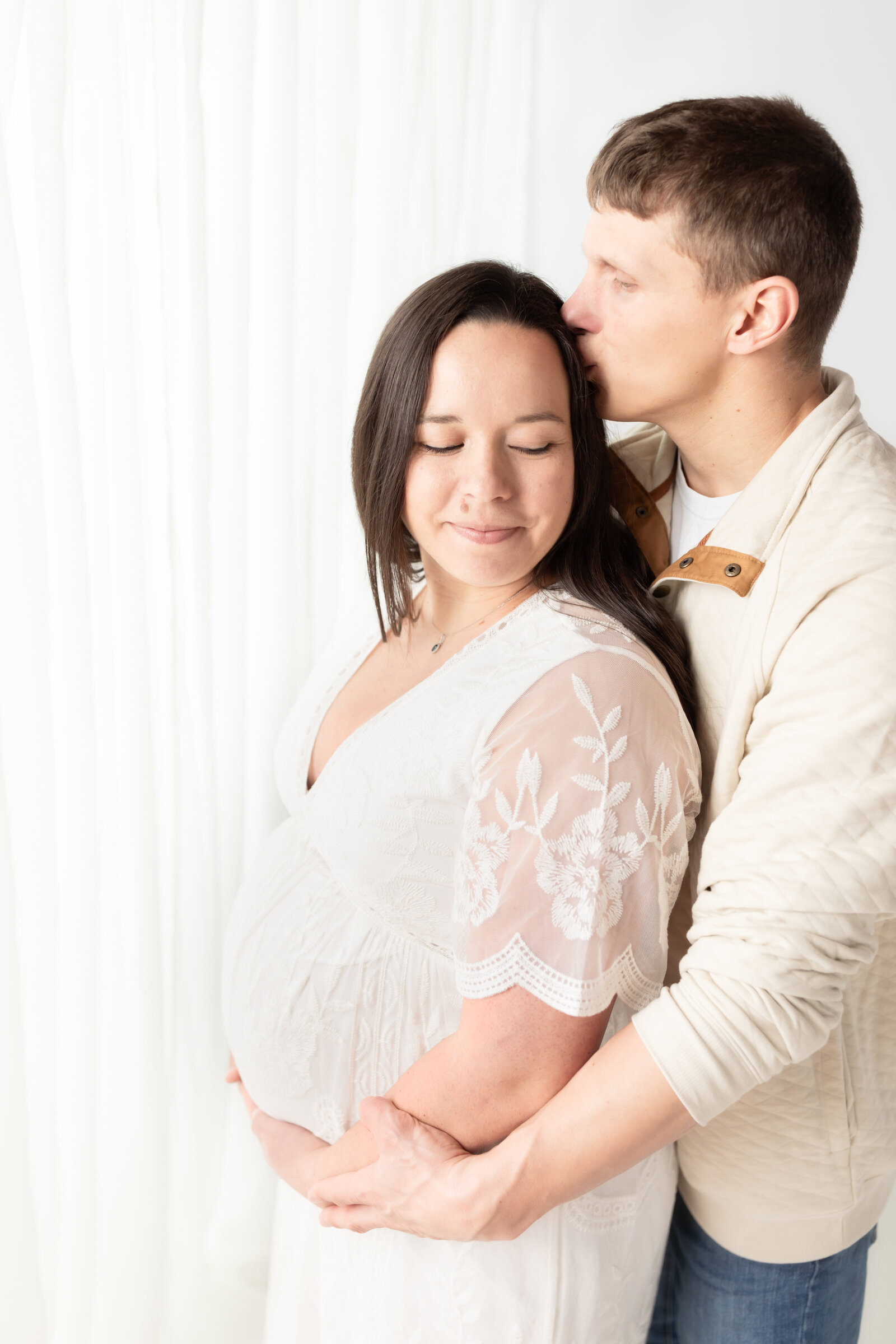 husband kissing wife holding pregnant belly for maternity photos
