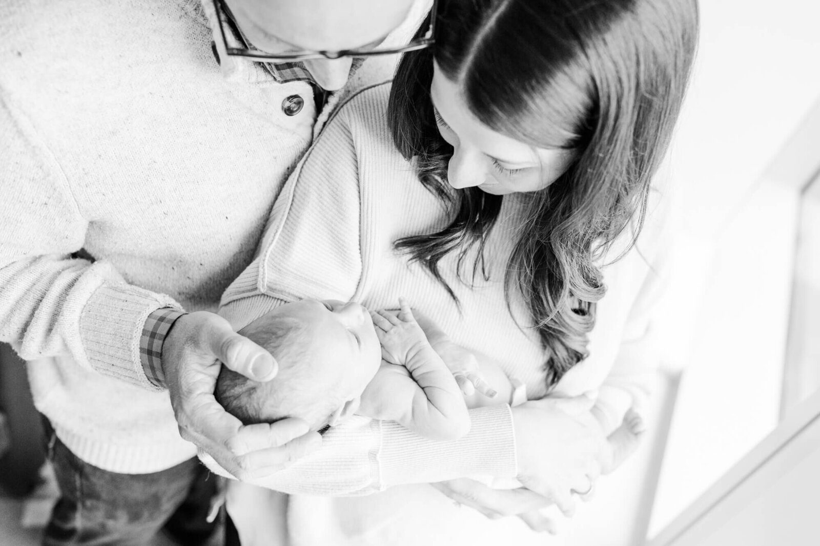 Black and white, taken from above, mom and dad lovingly observe the newborn in mom's arms