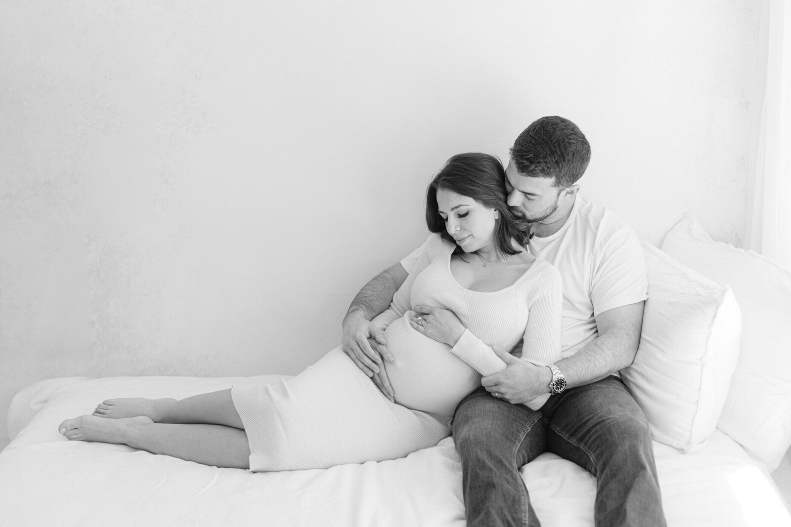 pregnant couple snuggled up on bed maternity photos cream dress mom holding belly