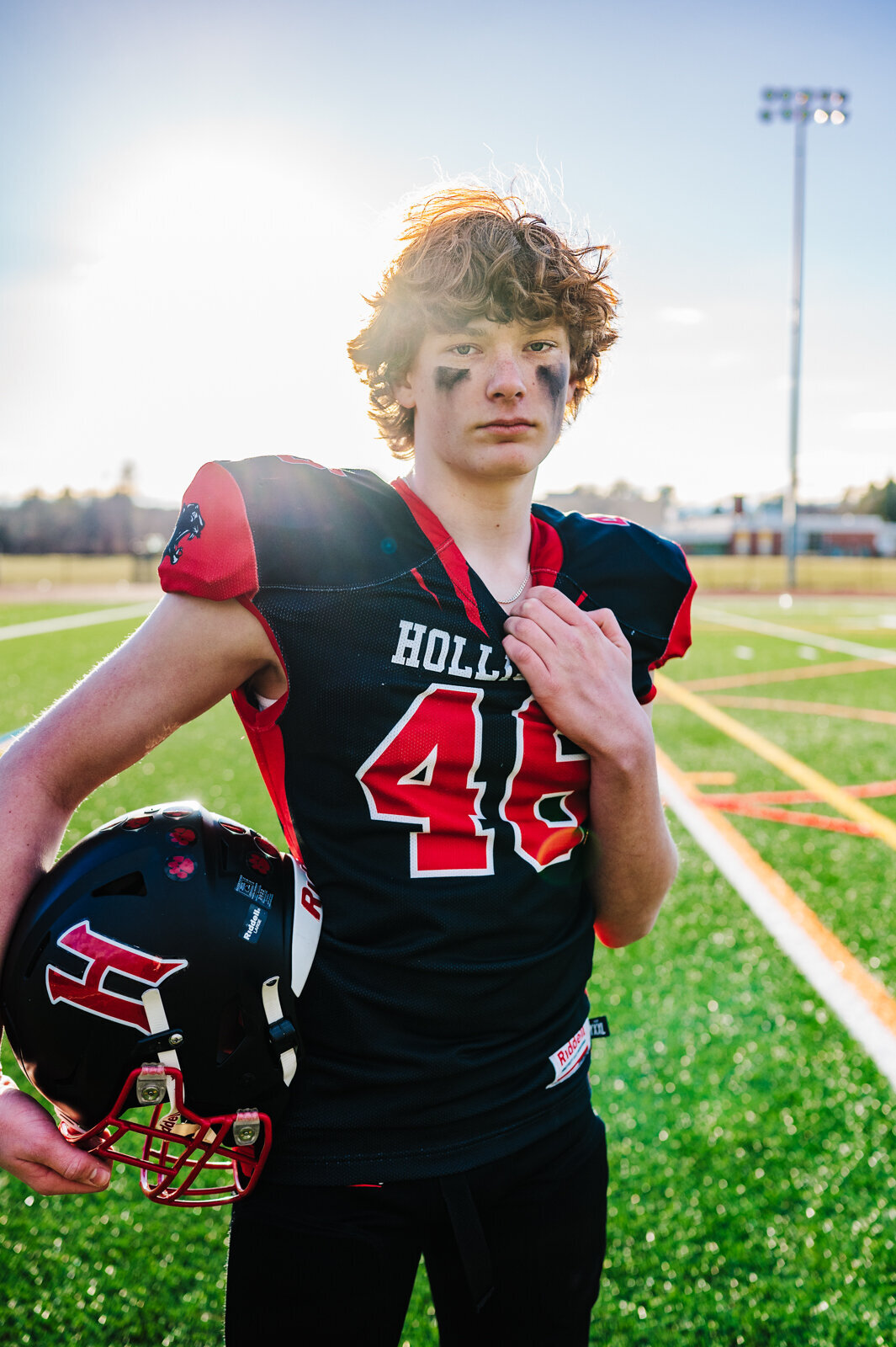 Boy wearing football jersey and pads holding a helmet for Boston sports photography