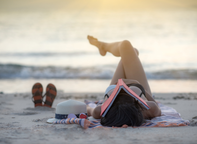 woman lying on beach relaxing at sunset with a book resting open on top of her face