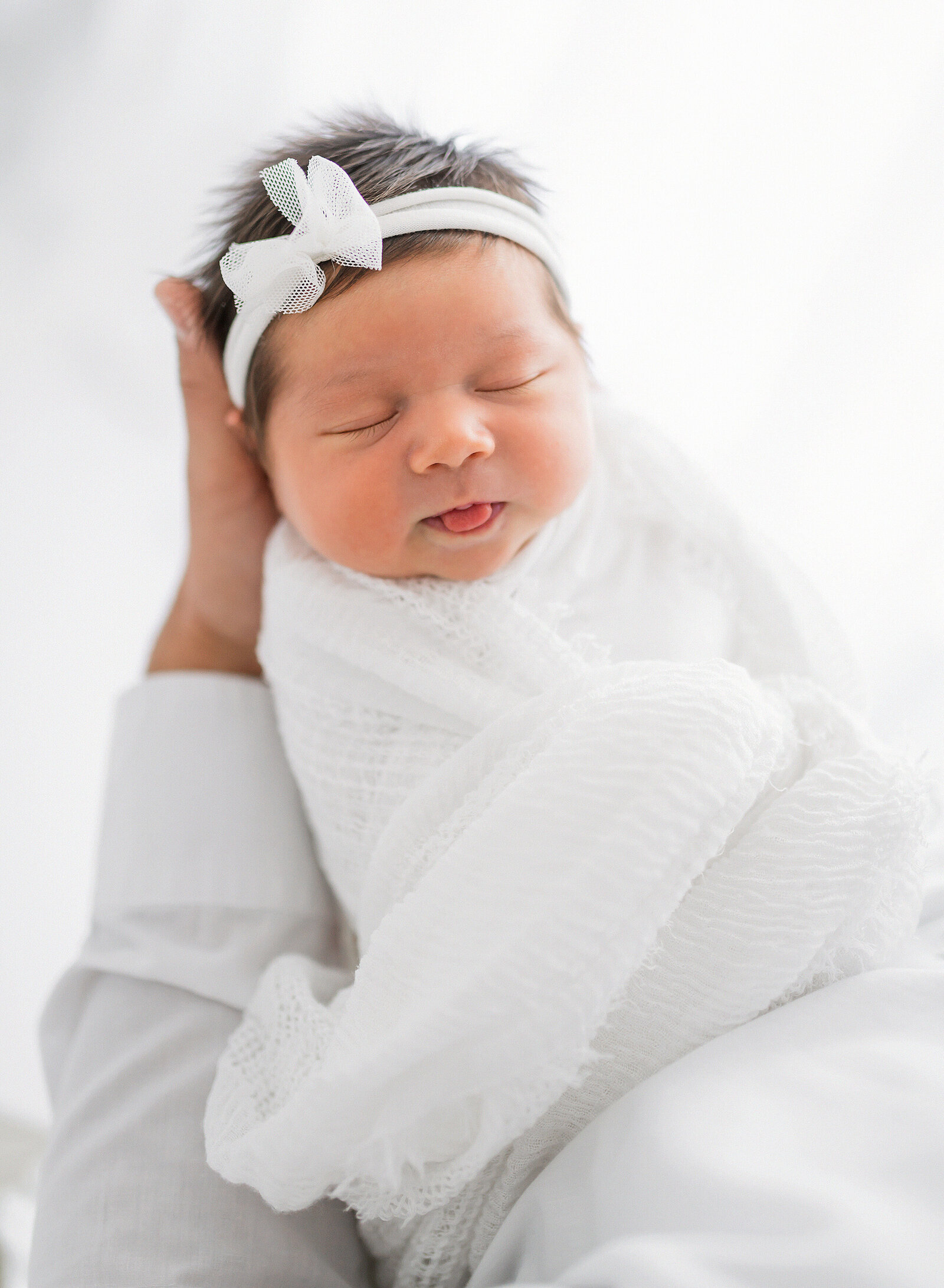 newborn wrapped in white wrap sticking out her tongue