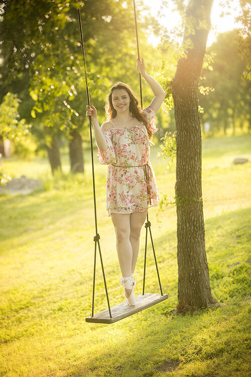 Senior girl stands on swing wearing toe shoes