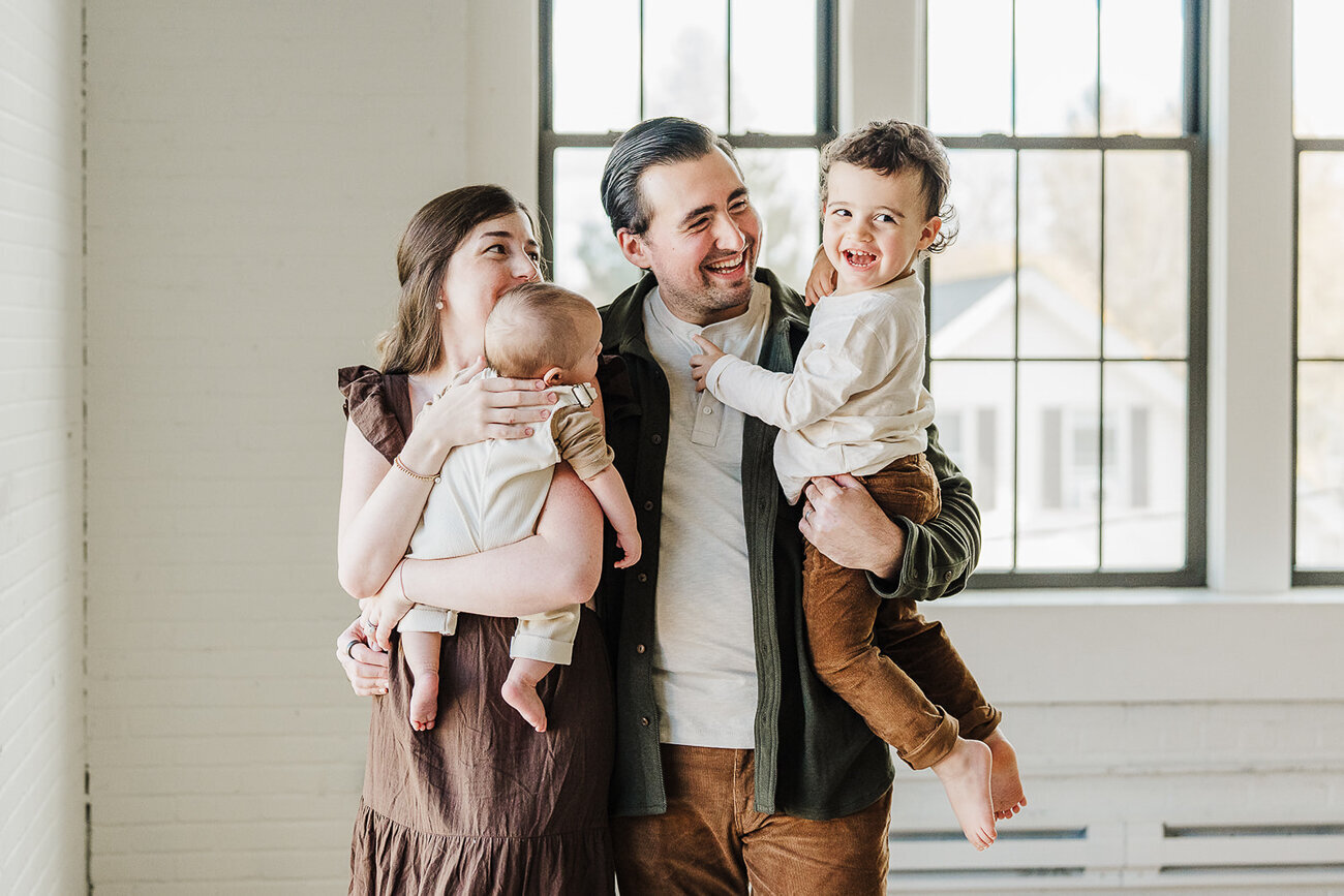 family with two sons laugh together in front of industrial windows