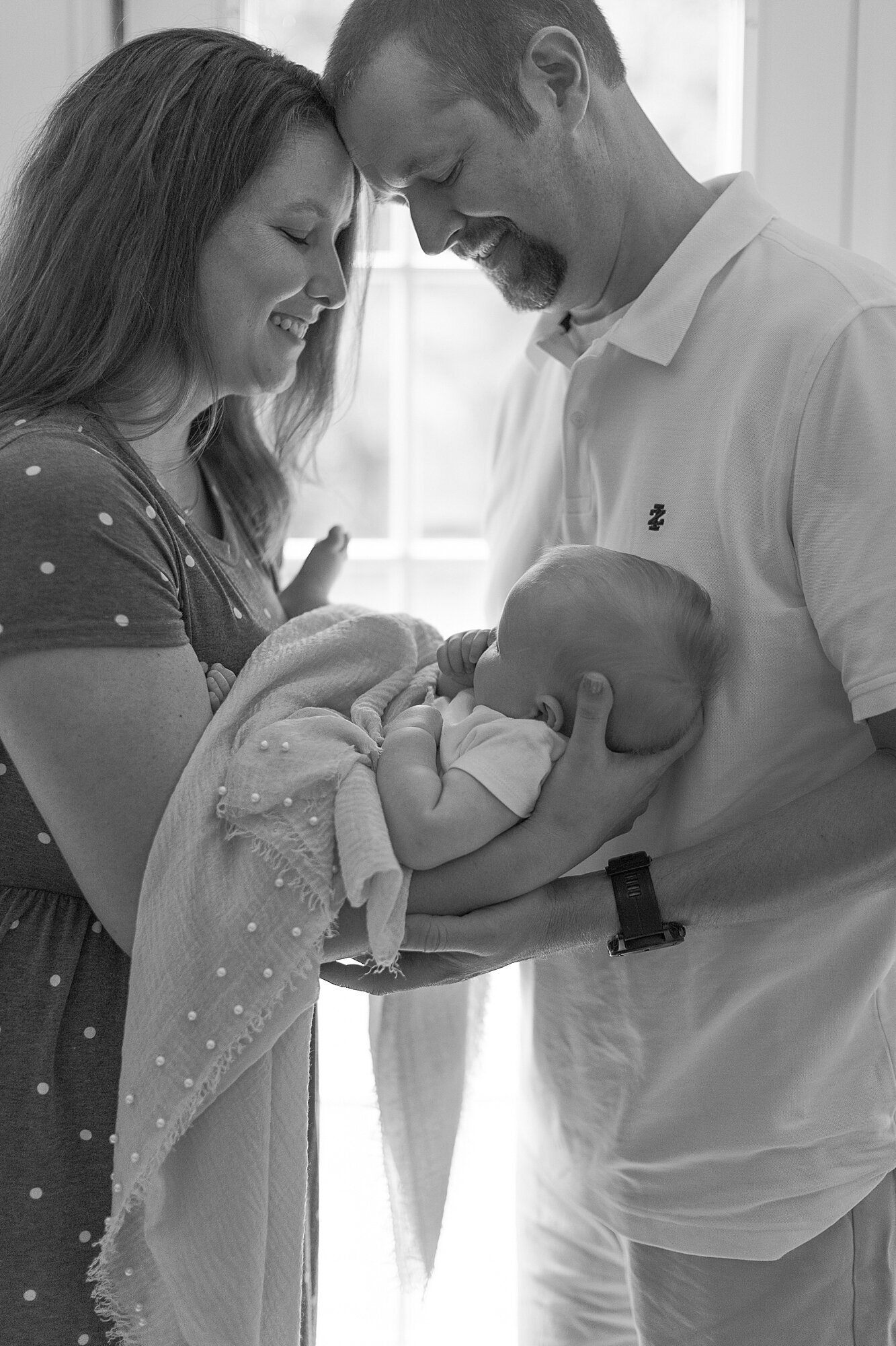 mom dad and baby in black in white looking at baby
