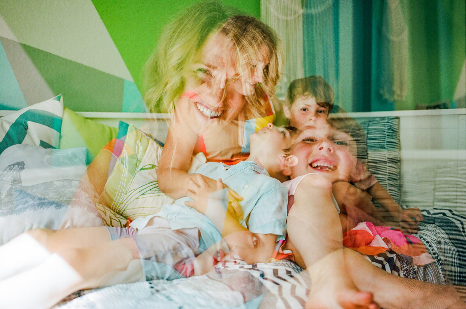 triple exposure of a mom with her two young sons sitting on a bed and smiling at each other