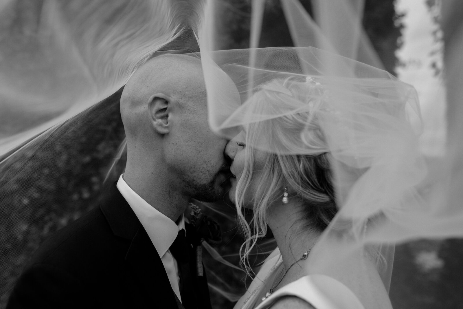 A bride and groom kiss under a windblown veil