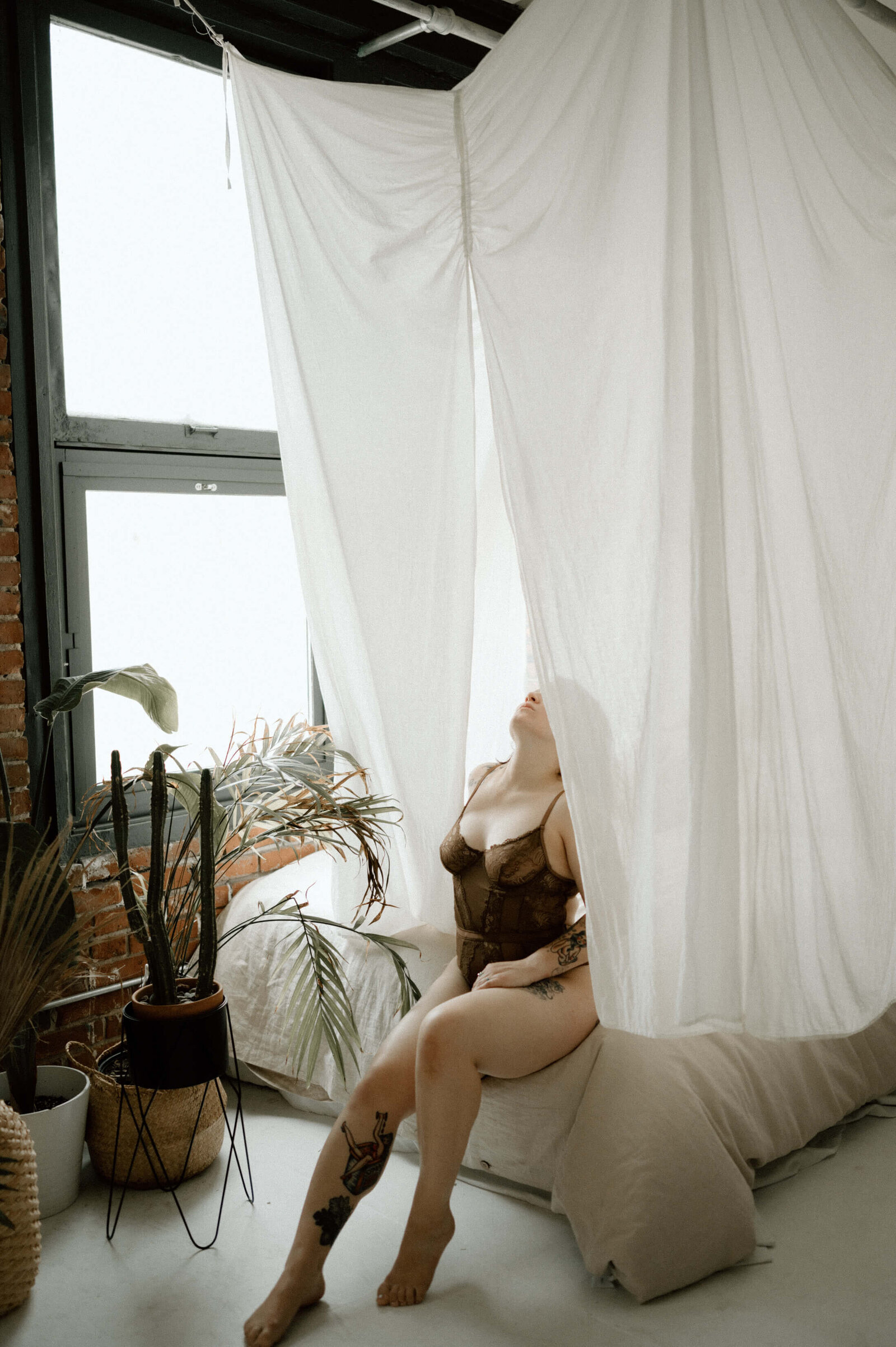 woman wearing a brown bodysuit lingerie with her face partially hidden by the bed canopy in seattle boudoir studio with Kayleen Lim Photography