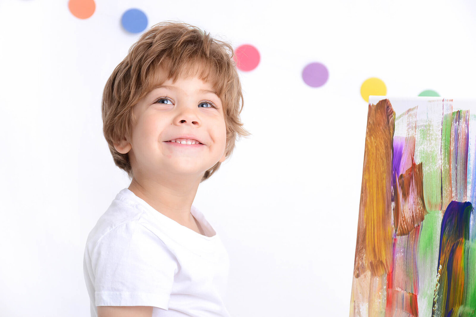boy smiles at the camera  with a painted canvas in the background
