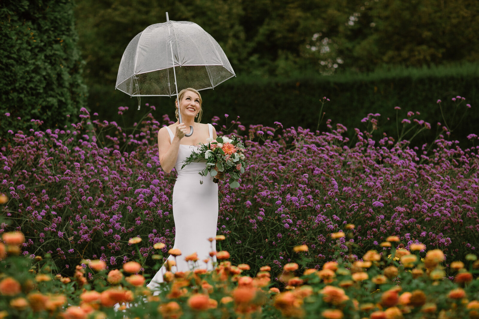 Bride standing in a colorful garden holding an umbrella.