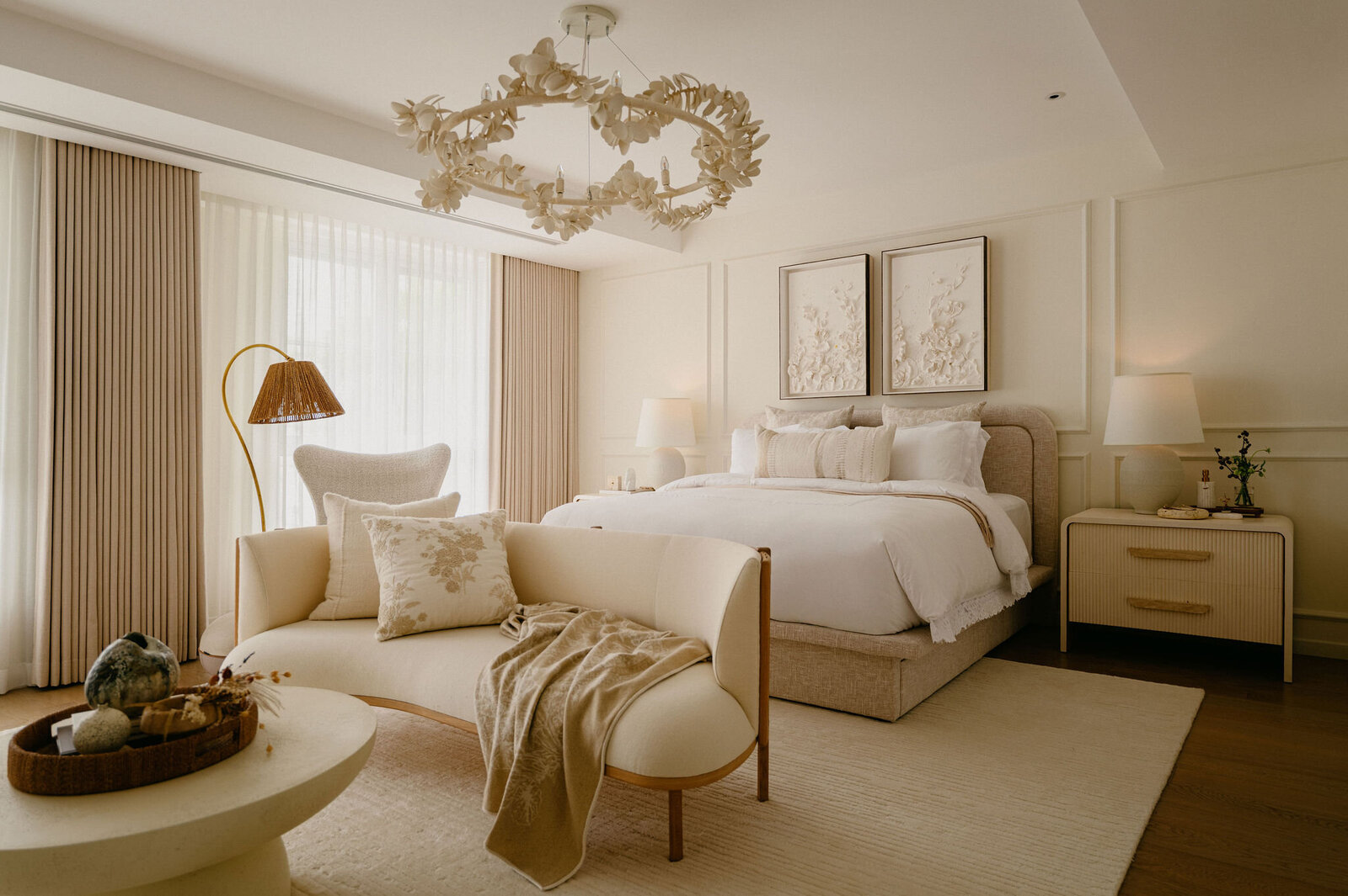 Master bedroom in soft neutrals featuring a sculptural chandelier, upholstered bed, and bespoke furniture layered with natural textures.