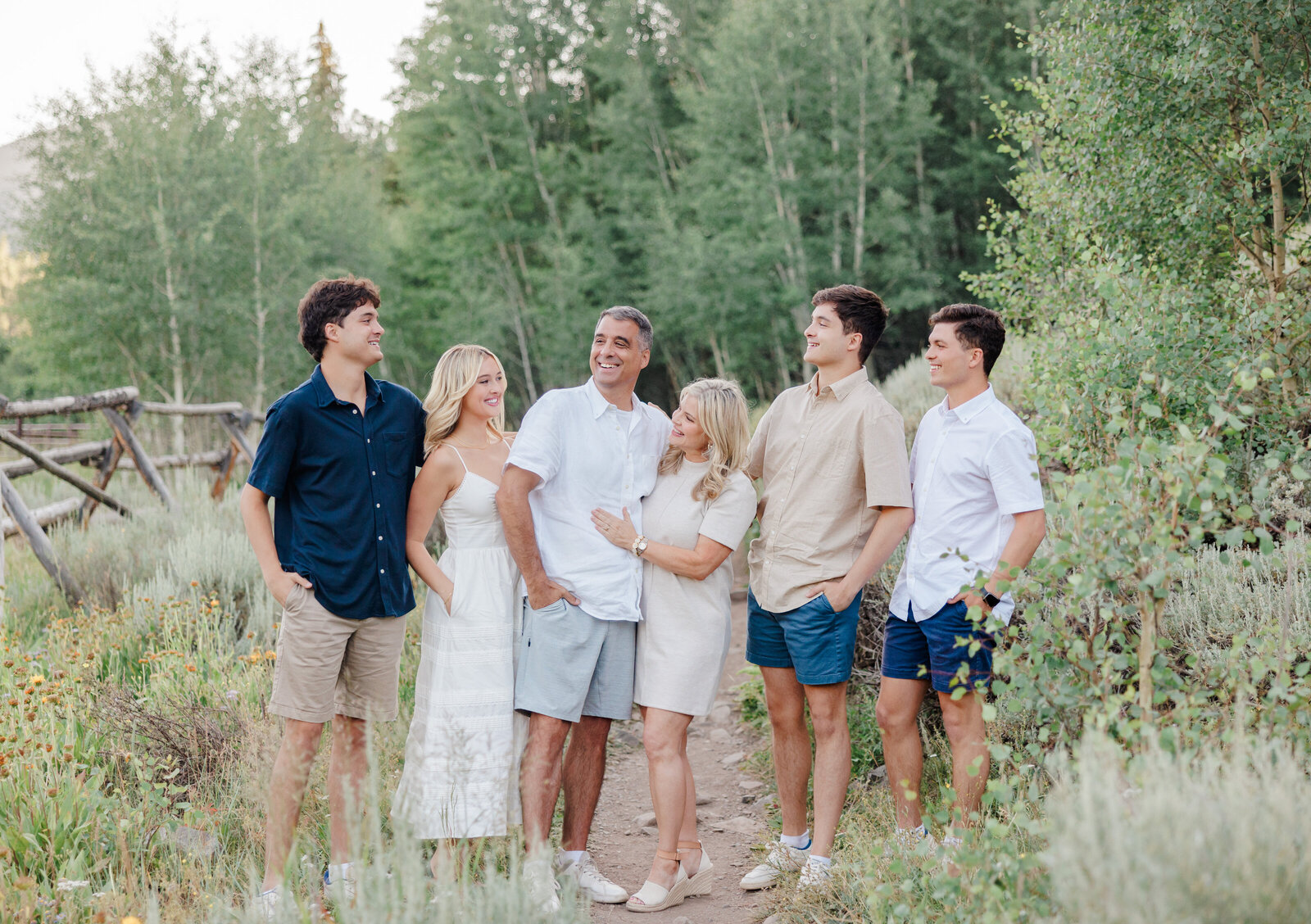 A family of two parents and their 4 adult children are standing closely together, smiling at each other. Taken by a Breckenridge photographer