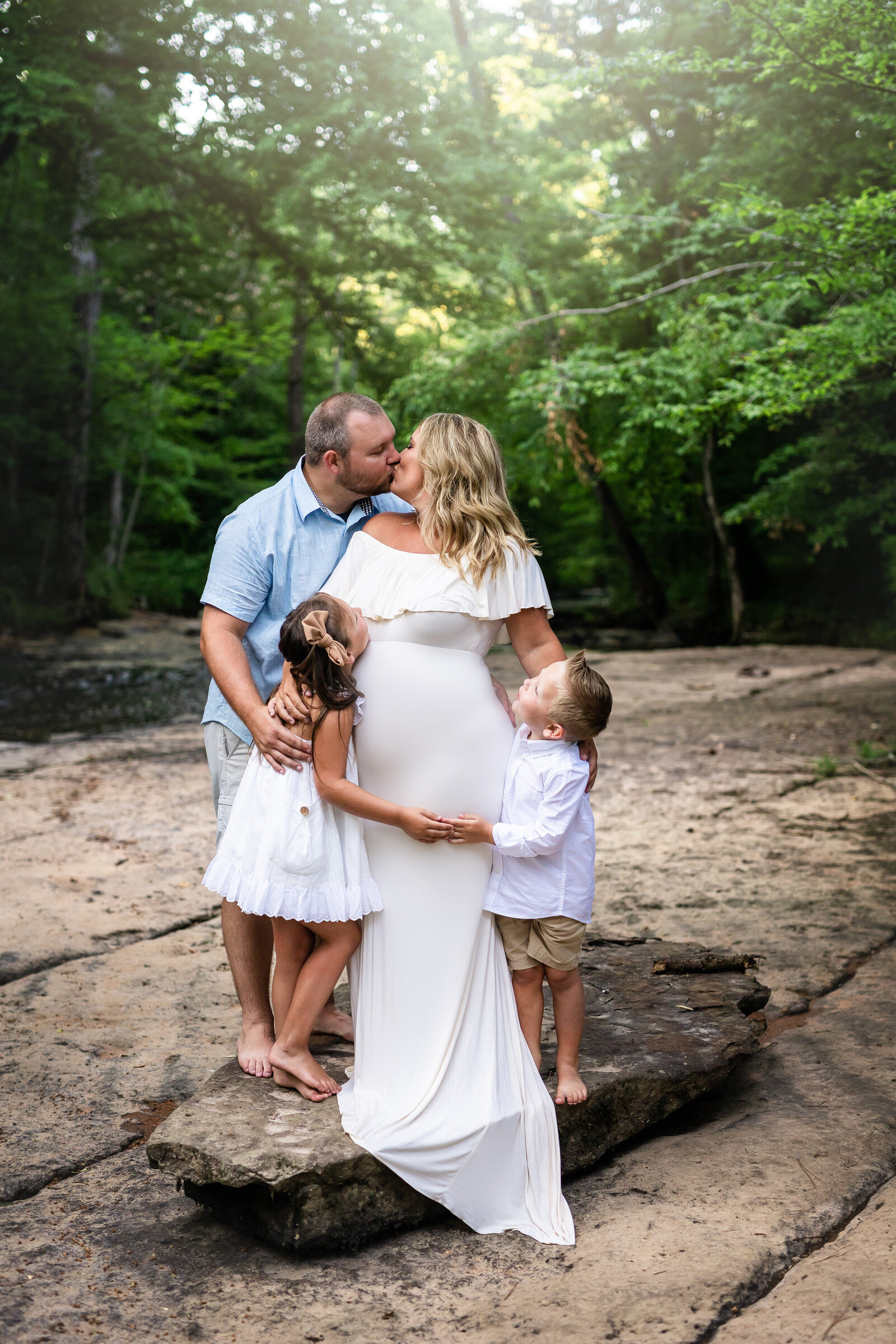 Family hugs mom during a maternity session by a creek located near Birmingham