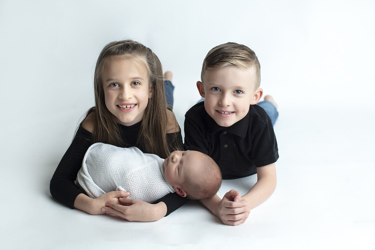 Siblings holding newborn brother.