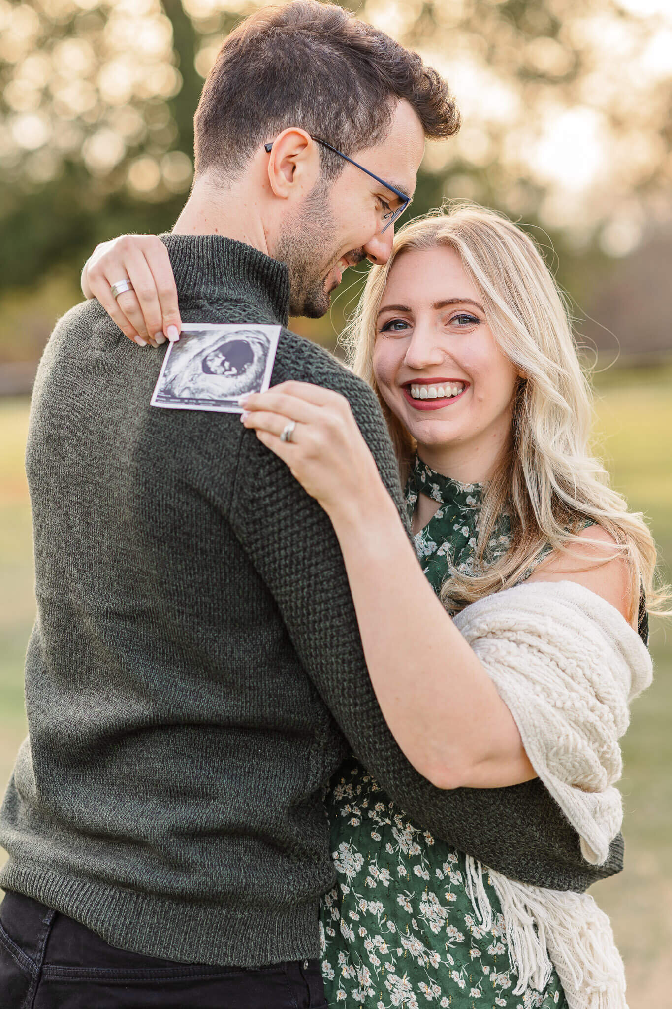 A pregnant woman hugging her husband and holding a sonogram behind his back..