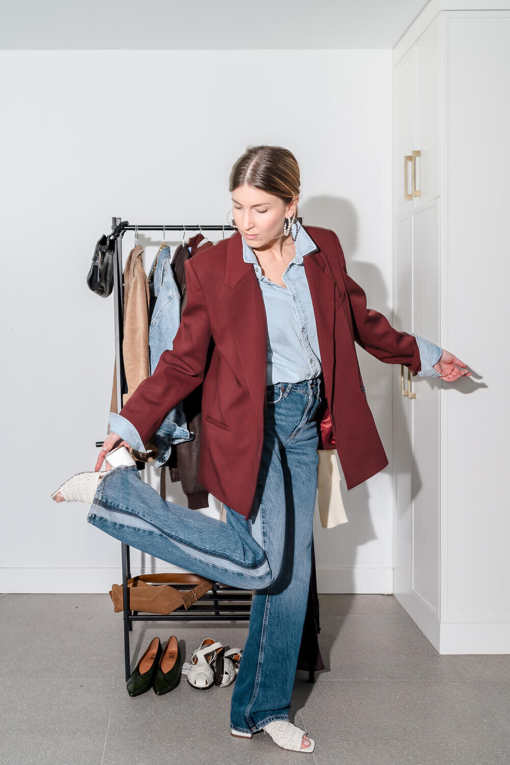 Wardrobe stylist in burgundy blazer and blue jeans adjusting her shoe