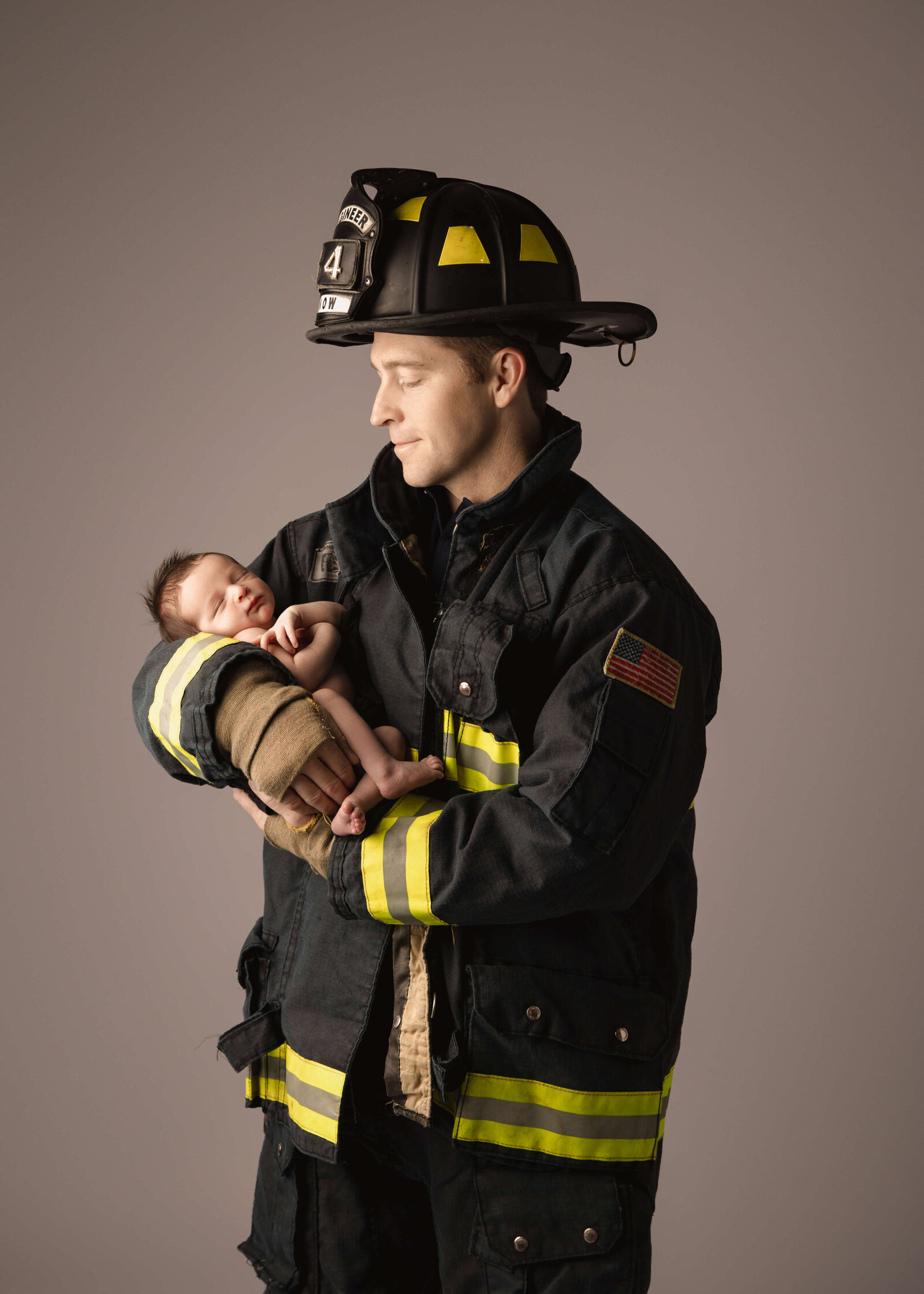 Dad wearing his firefighter uniform holding his new baby in studio session by Ashley Nicole Photography