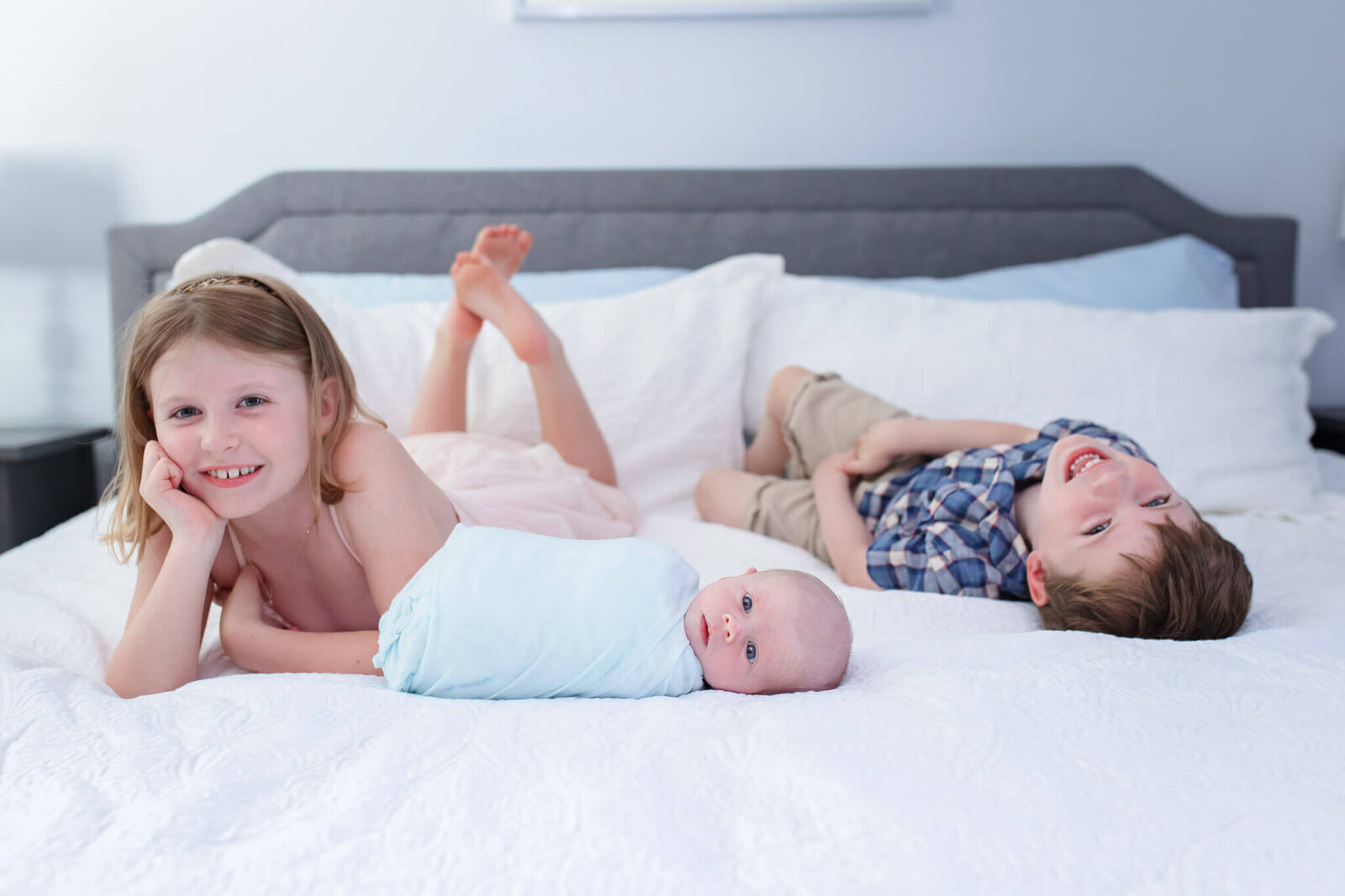 A big brother and sister laying in bed with their newborn brother.