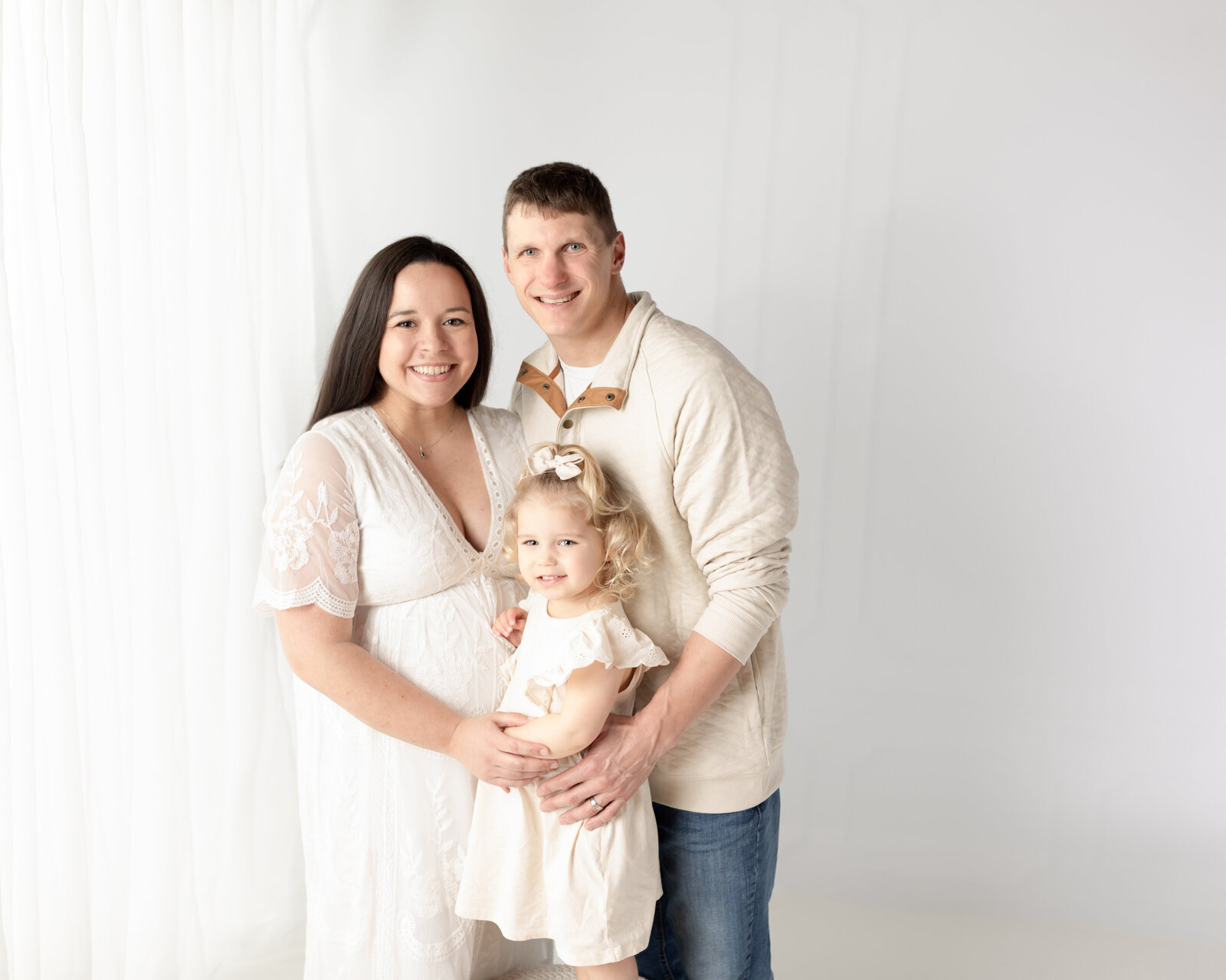 pregnant mother in white lace dress hugging daughter and husband for maternity photos