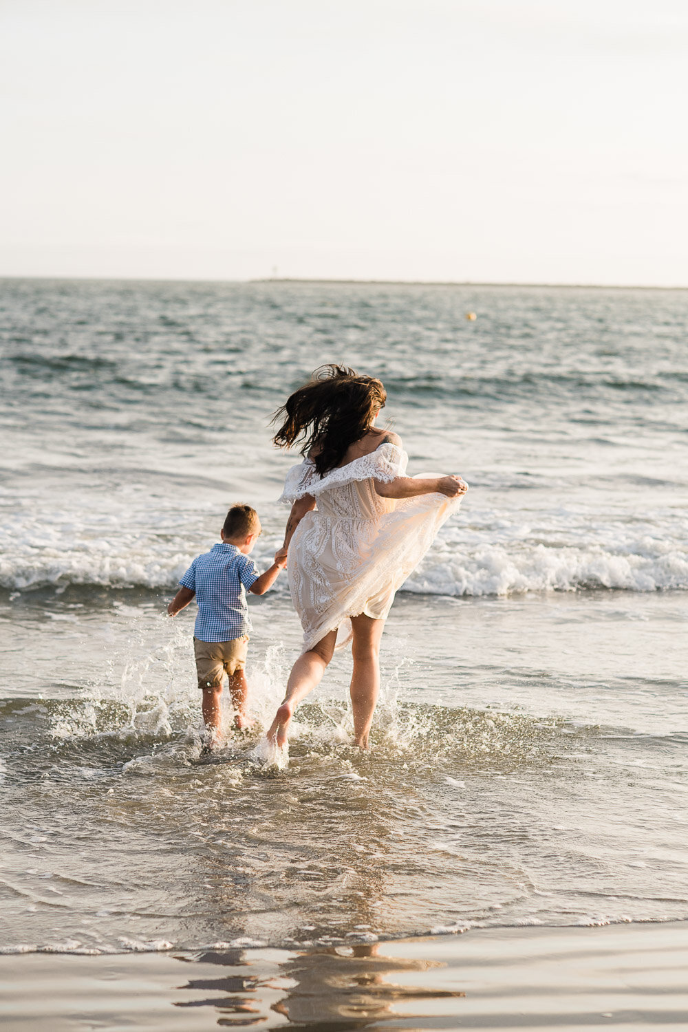 mom and son running in ocean on beach