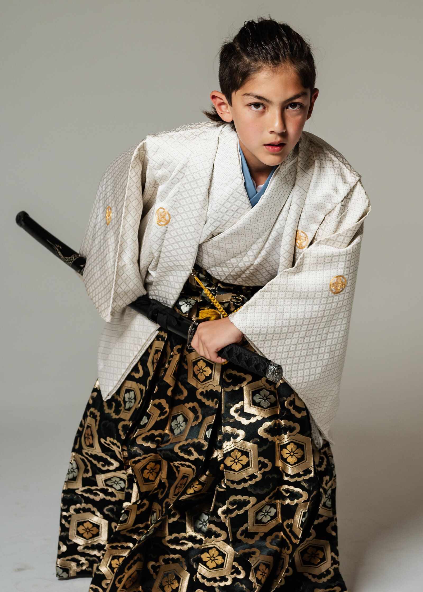 Boy in white kimono with gold crest and black-gold hakama posing with sword in samurai style | 卒業式 男の子 白着物 金紋 黒金袴 侍スタイル 刀