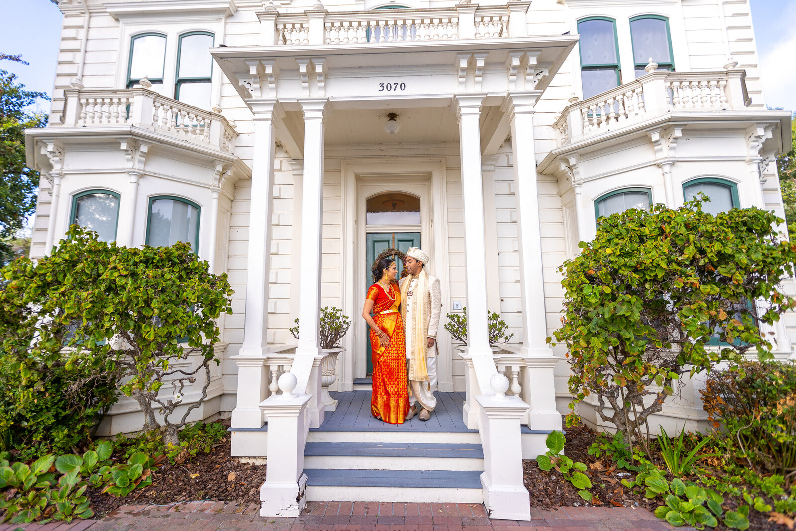 Indian couple stands in front of porch looking at each other in traditional indian wedding attire. Photo by Sacramento wedding photographer, philippe studio pro.