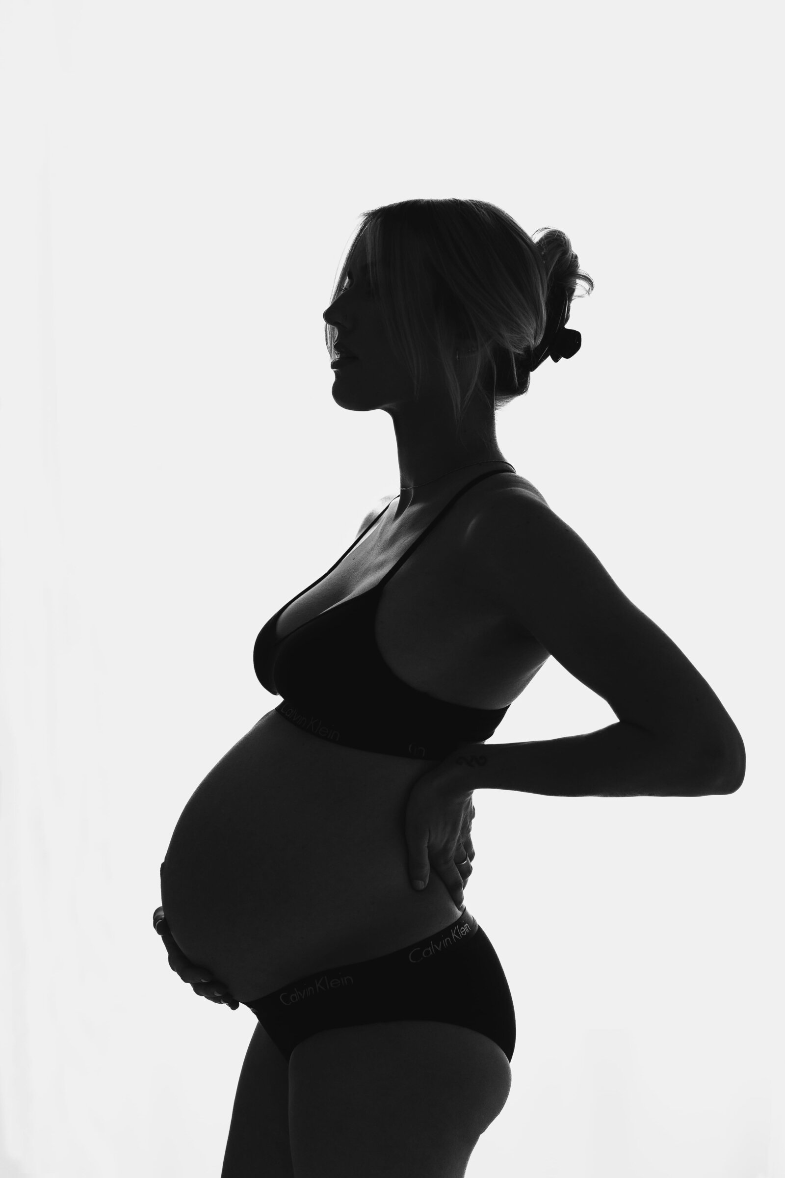 Pregnant woman posing in studio highlighting belly in black and white.