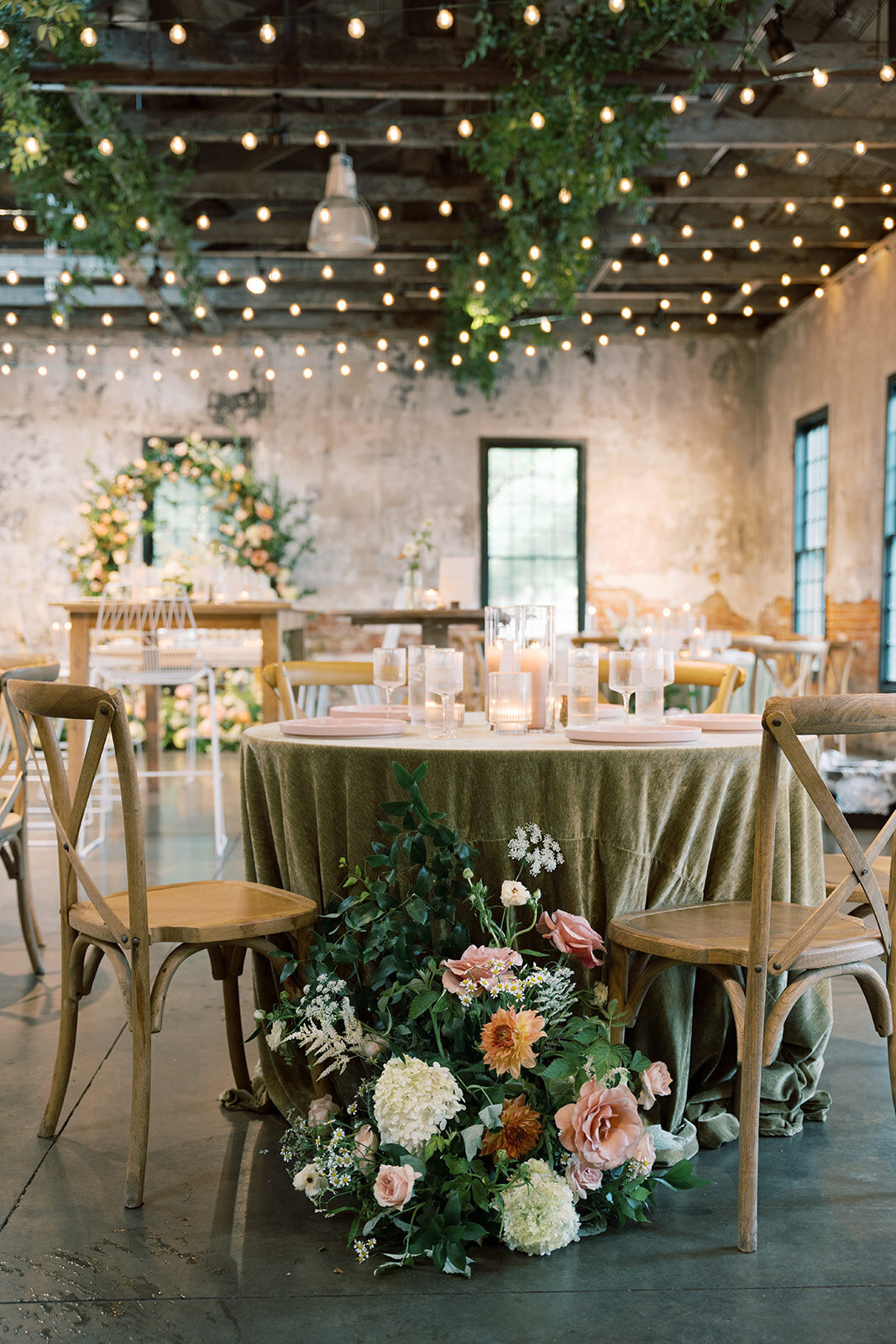Round table at reception in the Washington mill dye house with floral ground arrangement beside a chair with peach and blush garden roses, white hydrangea, daisies, white astilbe, and queen anns lace and peach dahlias.